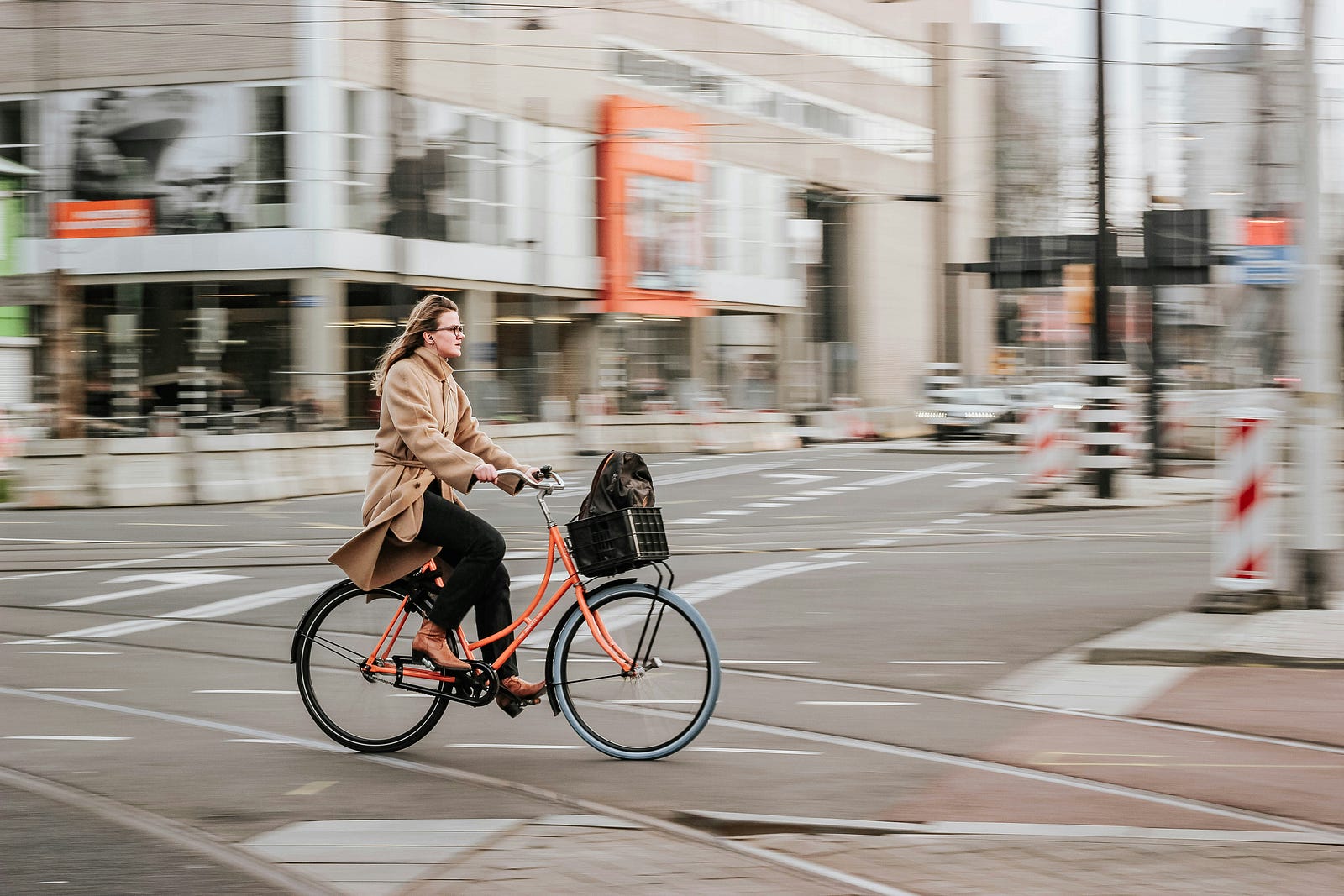 A woman rides a simple orange bicycle in the city.