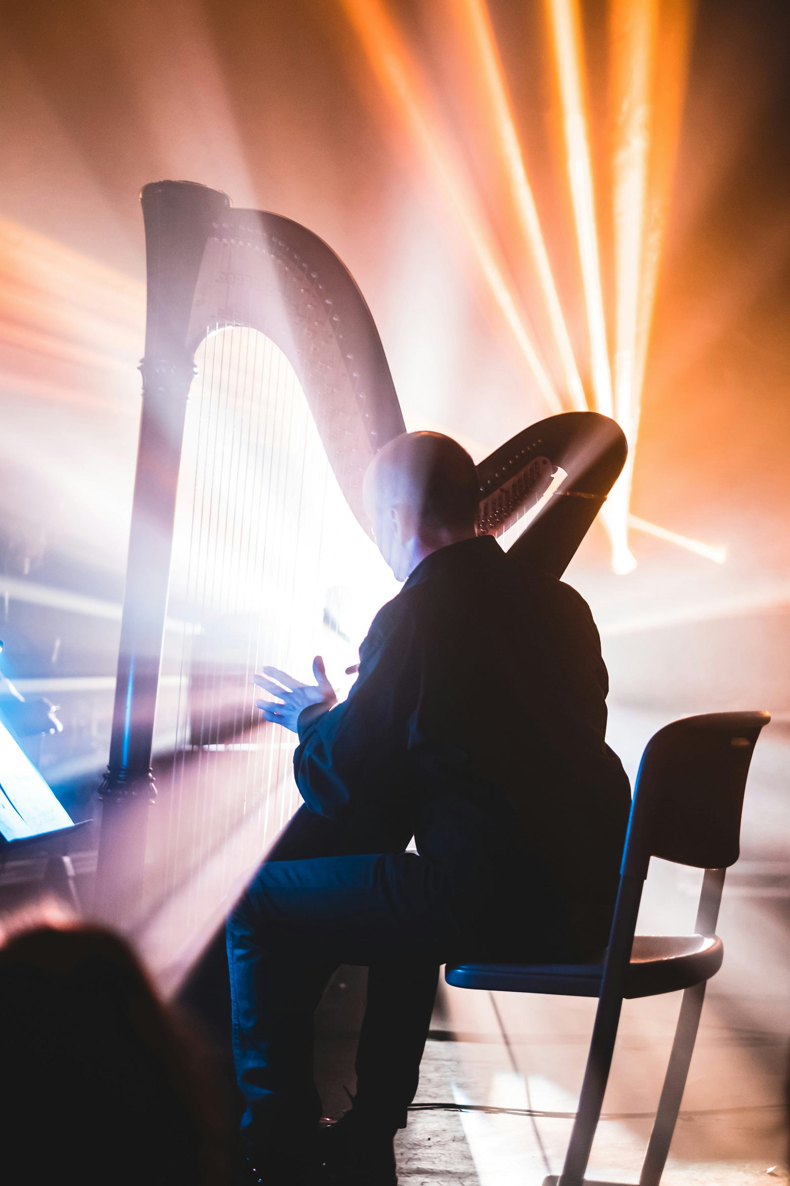 A harpist plays on stage with blaring lights in front of him.