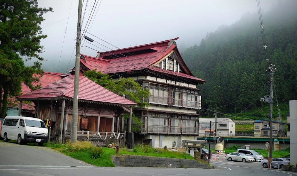 A giant wooden Japanese building with characteristic red roof and foggy Kamewari-yama (Mt. Kamewari) in the background.