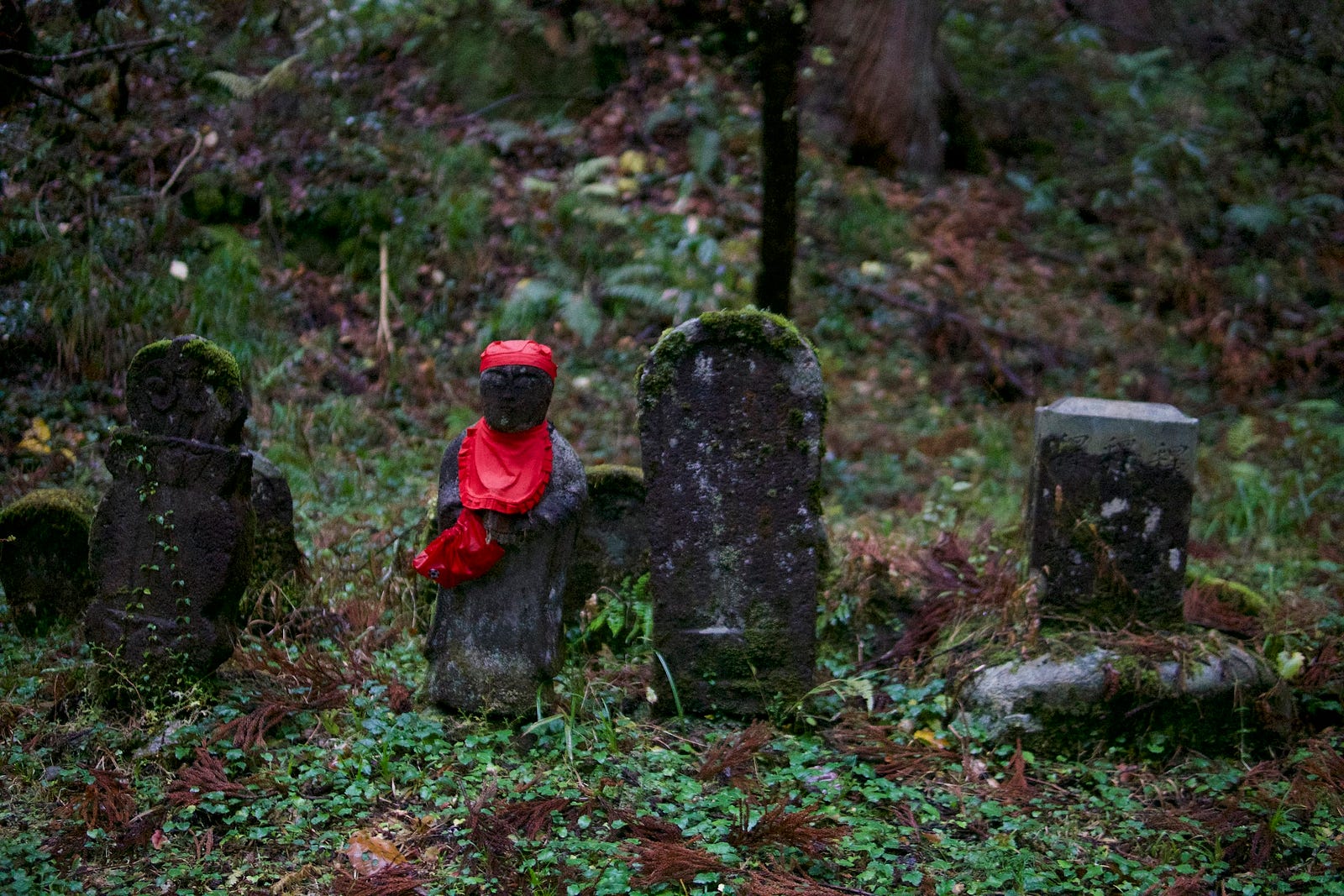 A statue of Jizo-sama with his characteristic red bib among other stone monuments on Haguro-san.