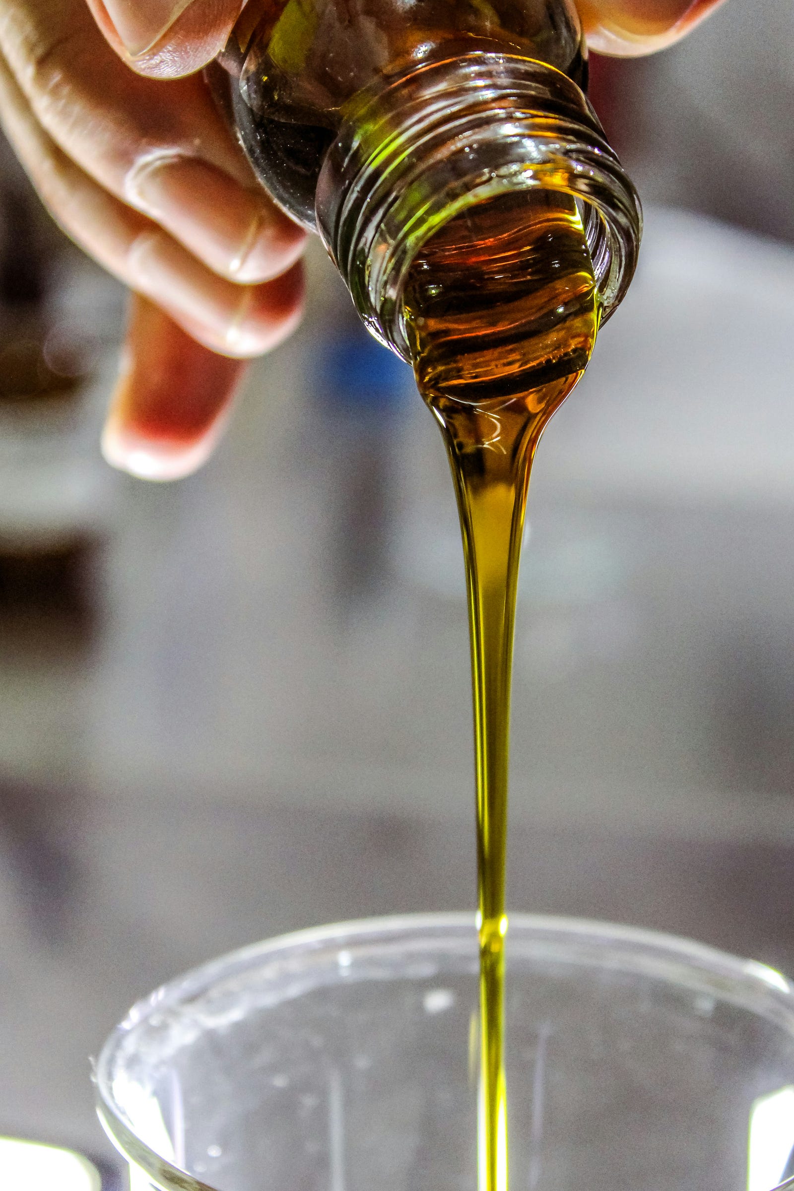 A hand is seen to pout olive oil into a cup.