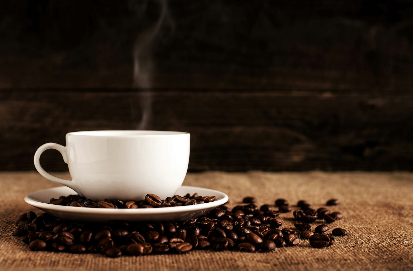 A white coffee cup and saucer, with coffee beans all around them.