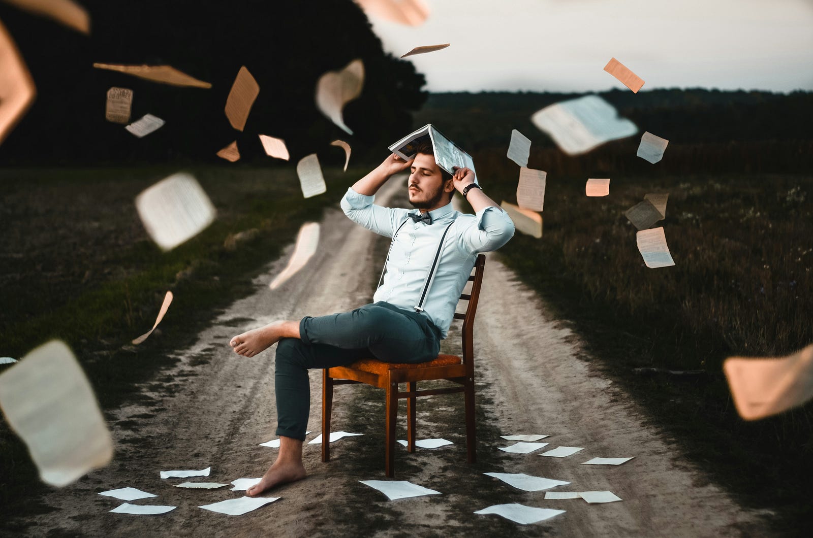 A man sits in a chair as papers fly around him in a room.