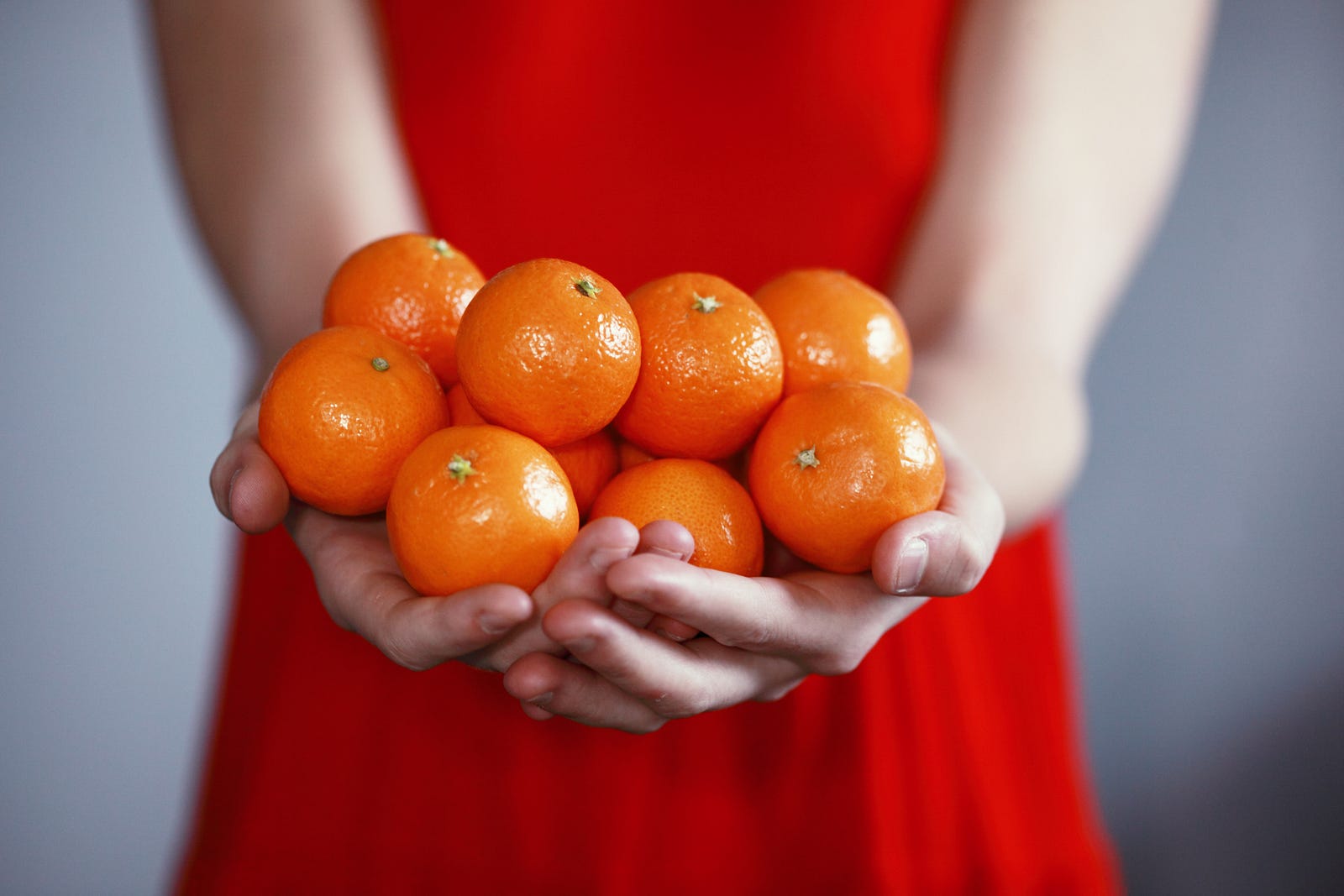 A woman holds 10 tangerines in her hands. We only see her torso, clad in a red dress. While I cannot tell you that tangerines reduce chronic brain disease, the fruit’s antioxidants may protect against dementia, Parkinson’s disease, and schizophrenia.