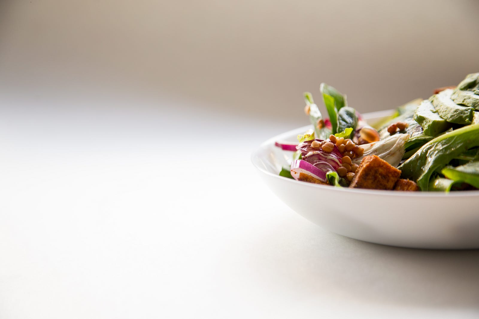 A white shallow bowl of salad is halfway into the image from the right. Intentional awareness involved with mindful eating helps individuals better understand their body’s signals of hunger and fullness and their emotional and psychological relationship with food.