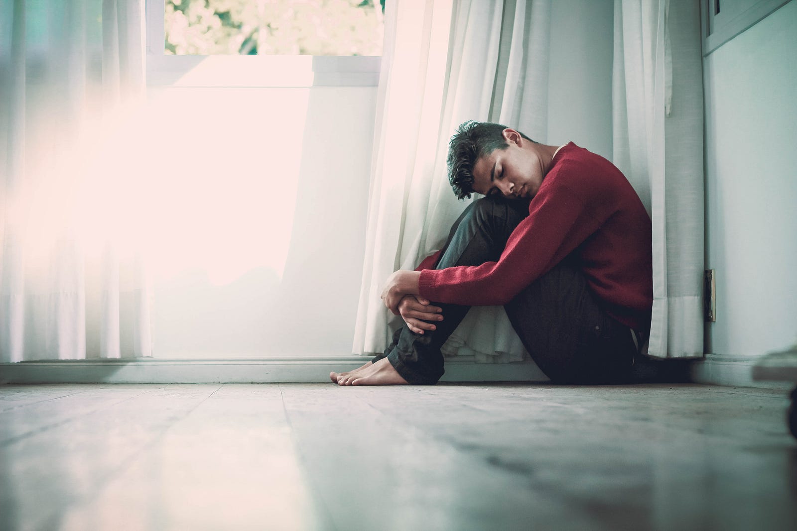 A young man sits on the floor. His head is bent forward to his knees. He appears sad. A loss of smell is associated with depression.