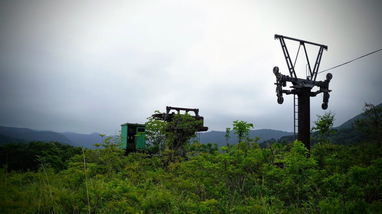 Fresh greenery surrounds the abandoned ski lift of Tsuchiyu-yama in Yamagata Prefecture with ominous grey sky in the background