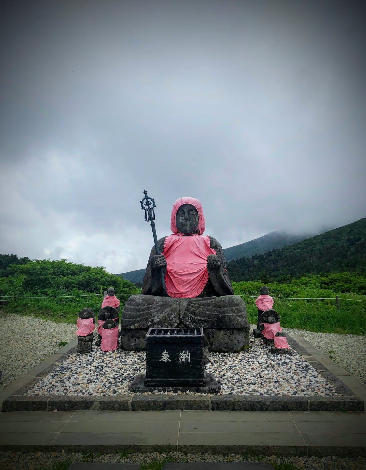 The Jizo statues of Jizo-dake, one of the peaks on Zao-san (Mt. Zao). The statues are wearing their characteristic red bibs, and are surrounded with a dark cloudy sky, and the fresh greenery of summer.