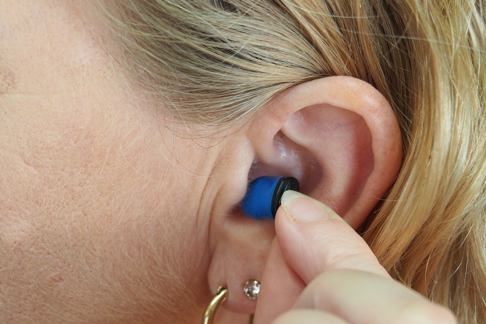 A close-up photo of a woman placing a blue hearing aid into her left ear. Studies suggest that treating hearing loss may help mitigate cognitive decline, reducing the risk of conditions like dementia and Alzheimer’s disease.