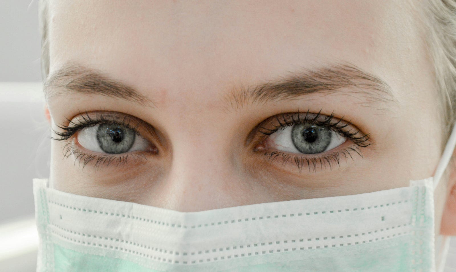 A close-up view of a female health professional staring at us. She dons a paper surgical mask.
