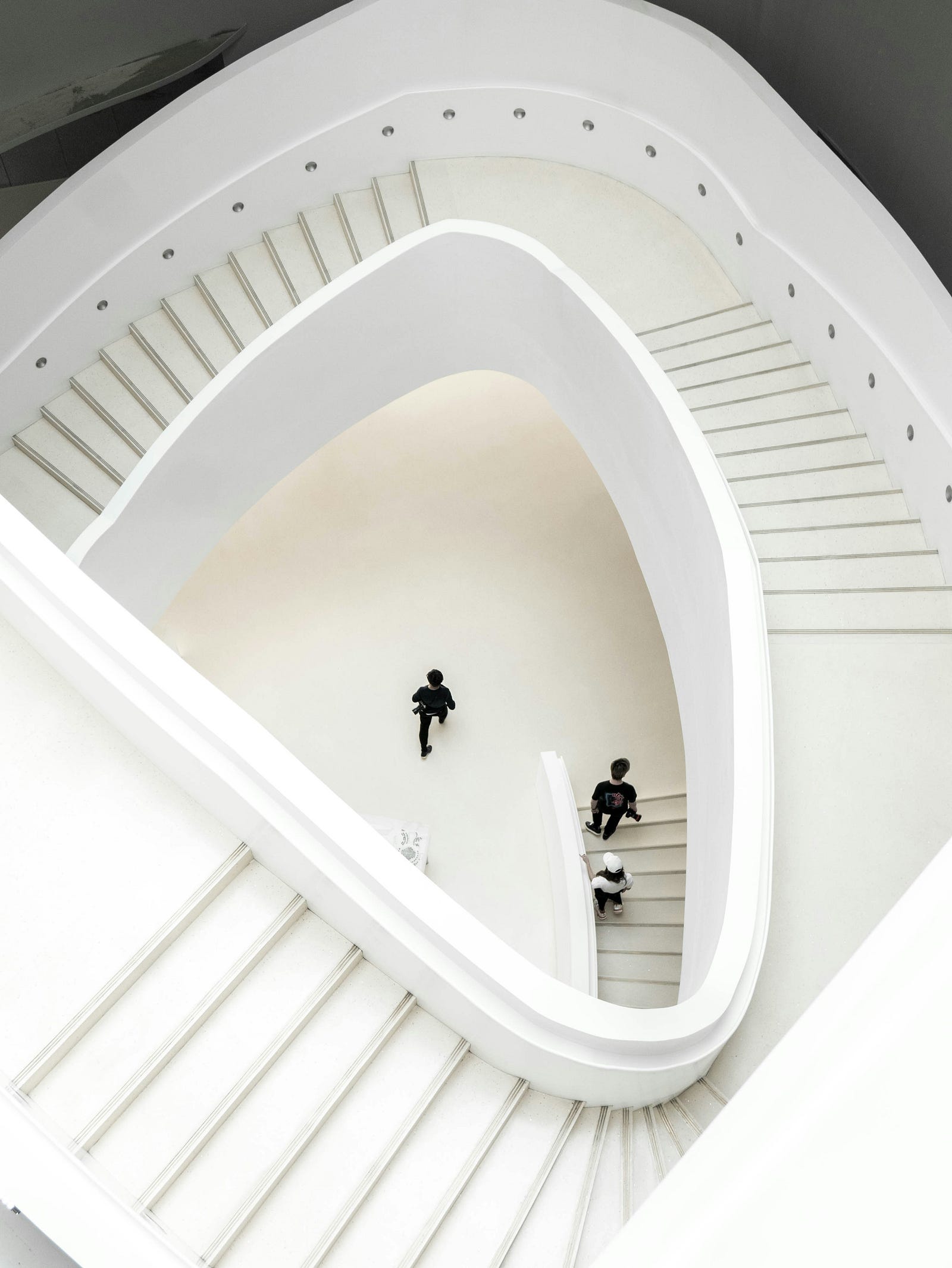 An overhead view of winding white stairs, with three individuals walking below. Exercise snacks (such as taking the stairs instead of an elevator) can help with weight maintenance.