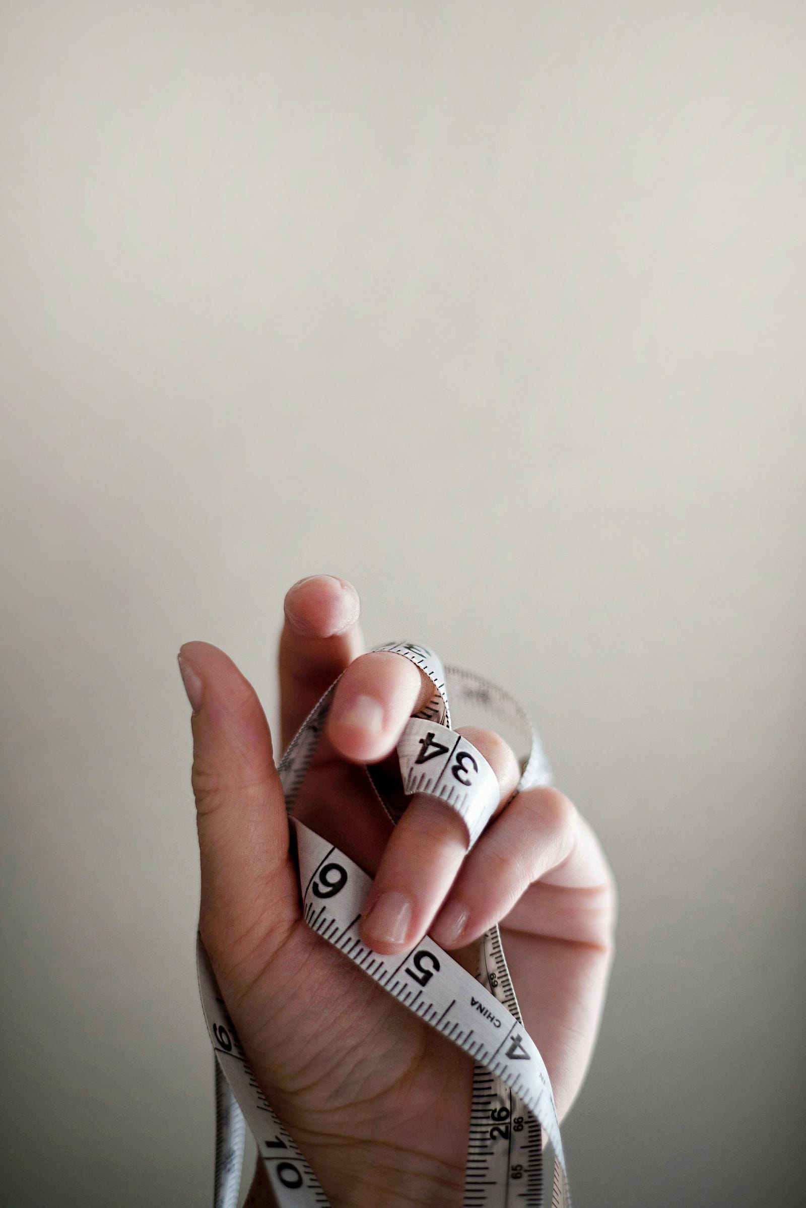 A tape measure weaves between the fingers of an upheld hand.