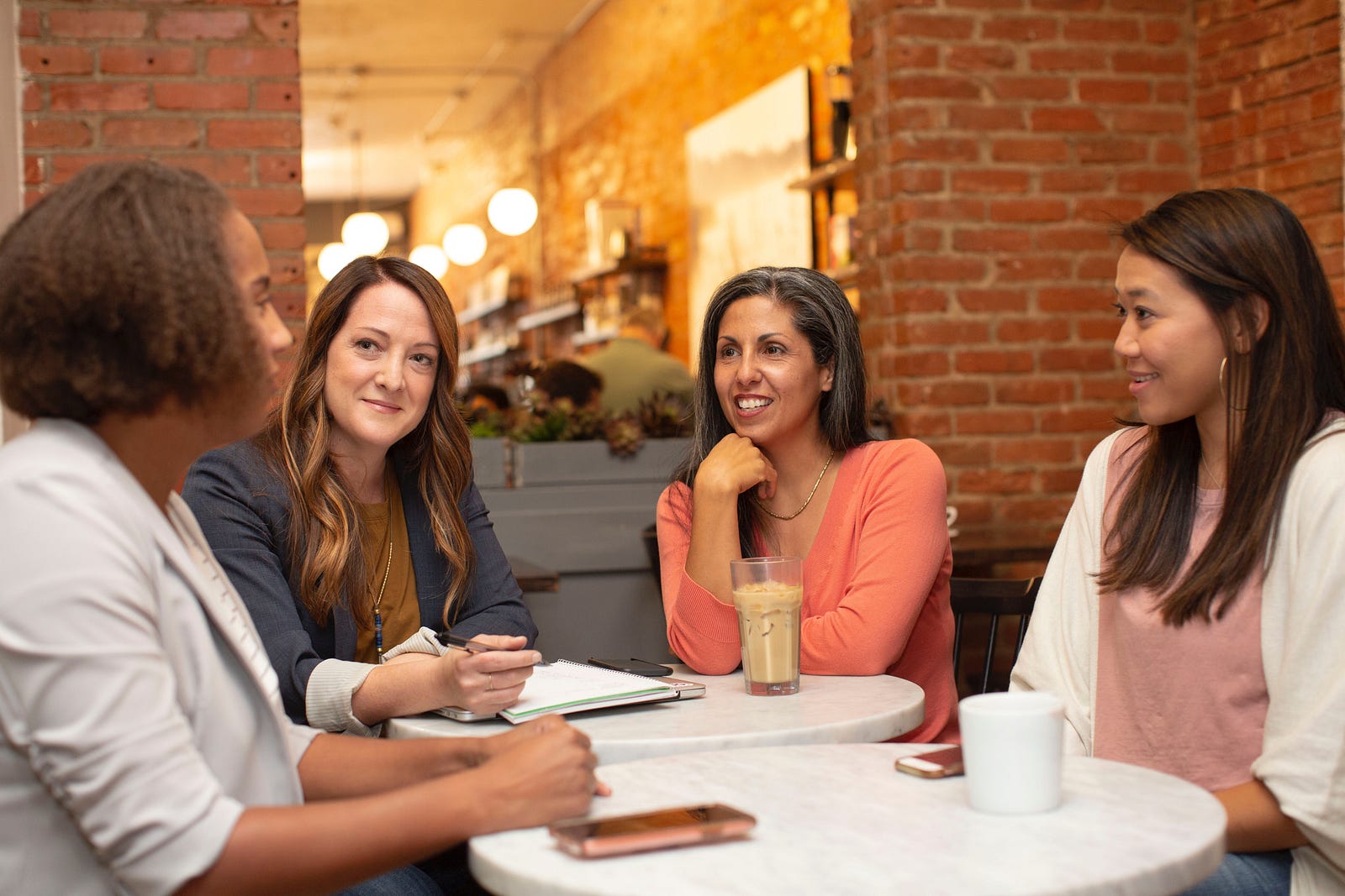 A group of four women (of various ages and ethnicities) sit at a coffee shop table. Mammography screening cuts the risk of dying from breast cancer nearly in half.