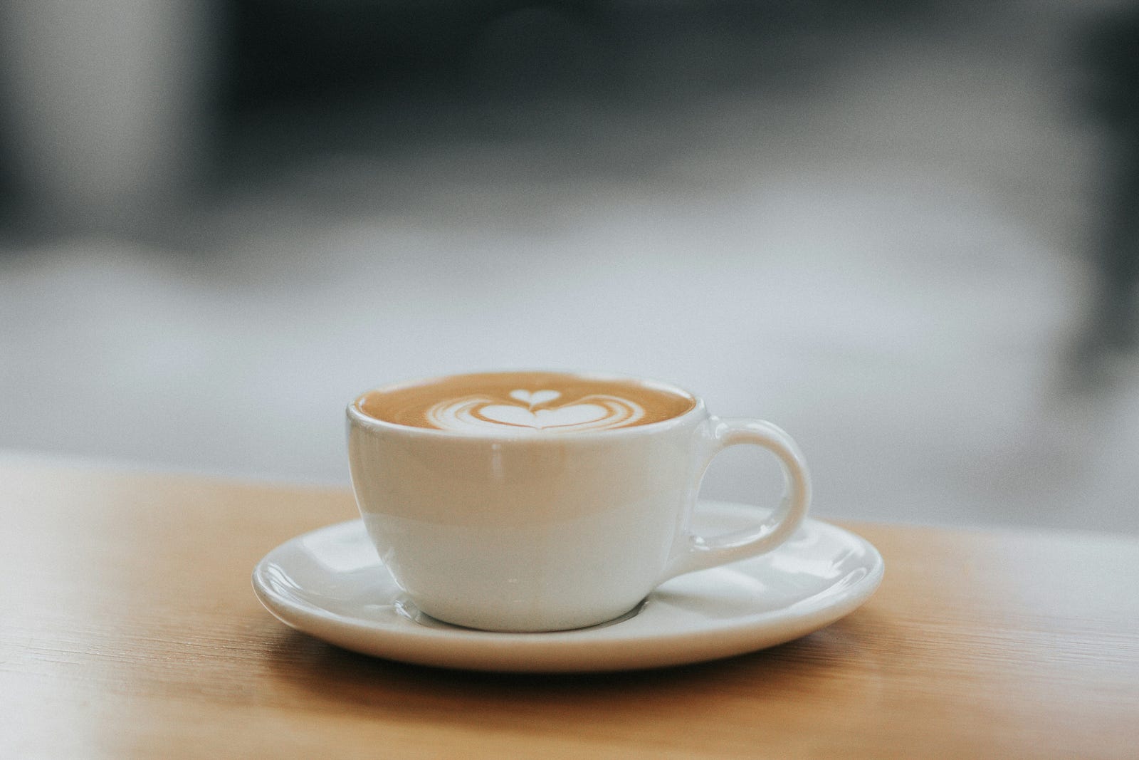 A white saucer, with a white cup filled with a cafe latte.