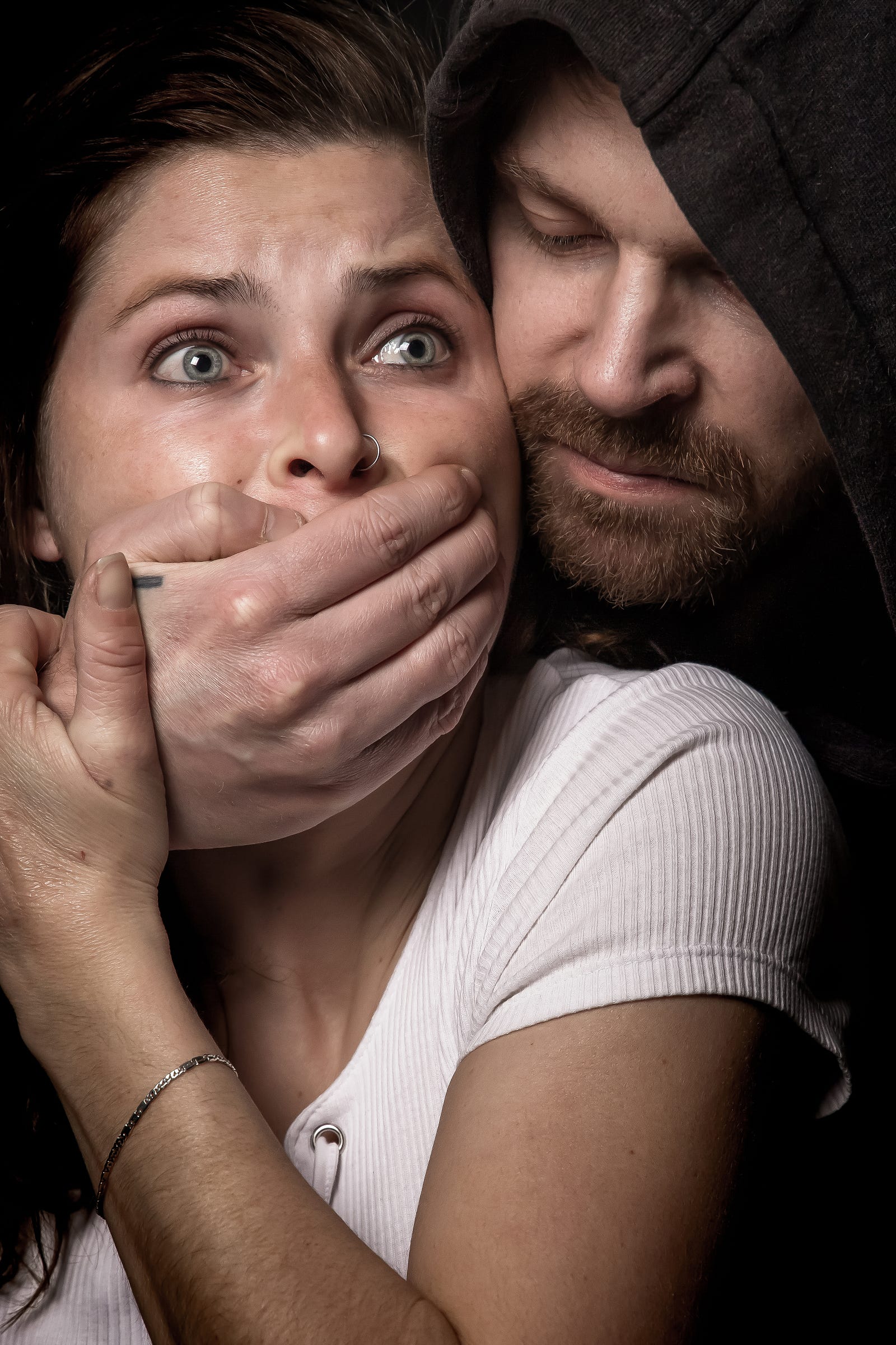 A hooded man covers the mouth of a female kidnap victim.