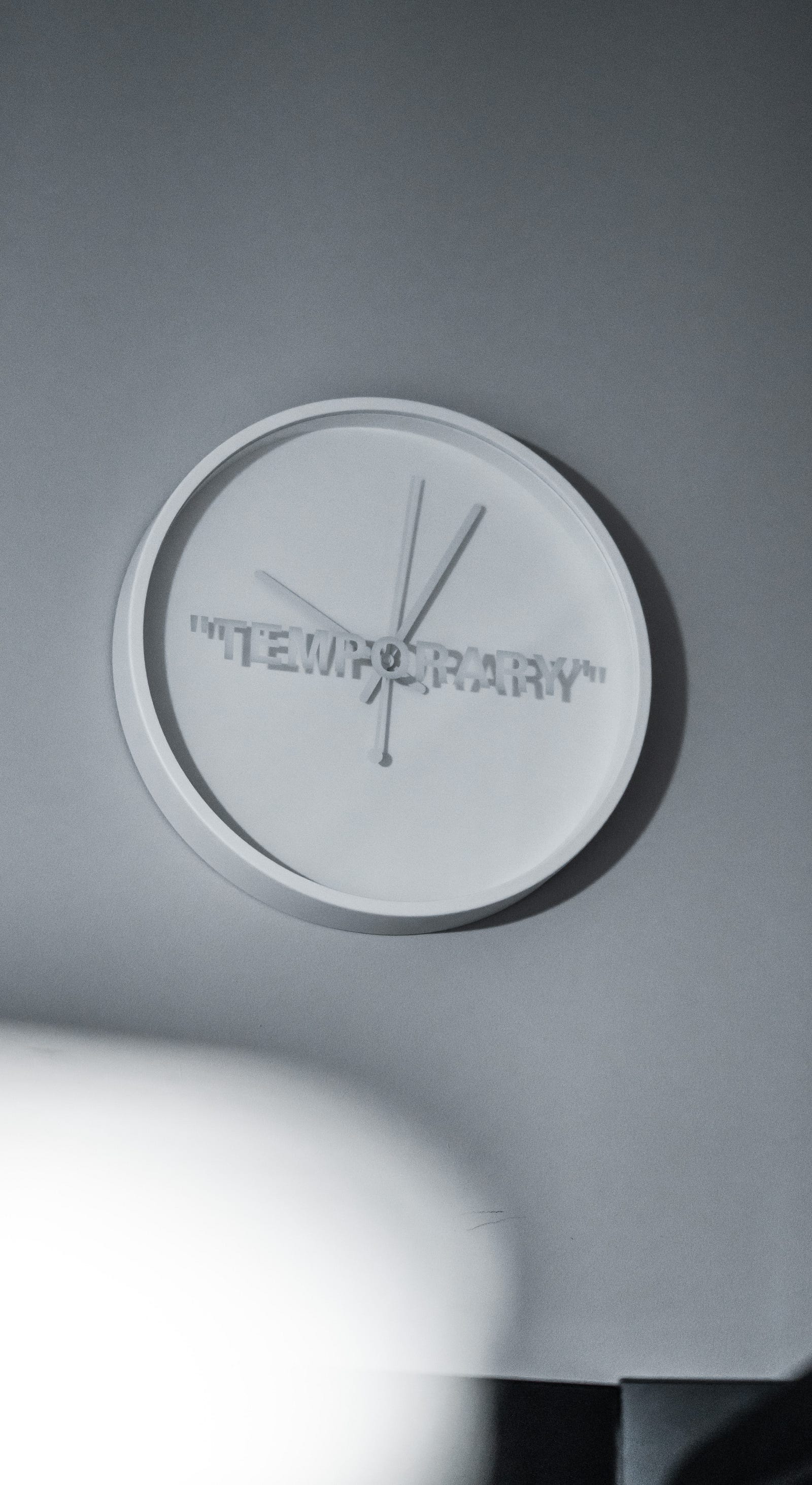 White clock on a white wall. The clock contains the word temporary