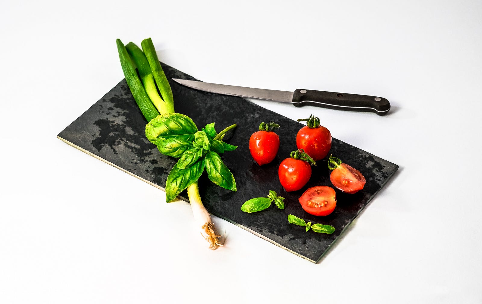 A cutting board (black) with small tomatos and a few leafy greens. A Mediterranean-style diet is associated with brain tangles and plaques that are associated with Alzheimer’s.