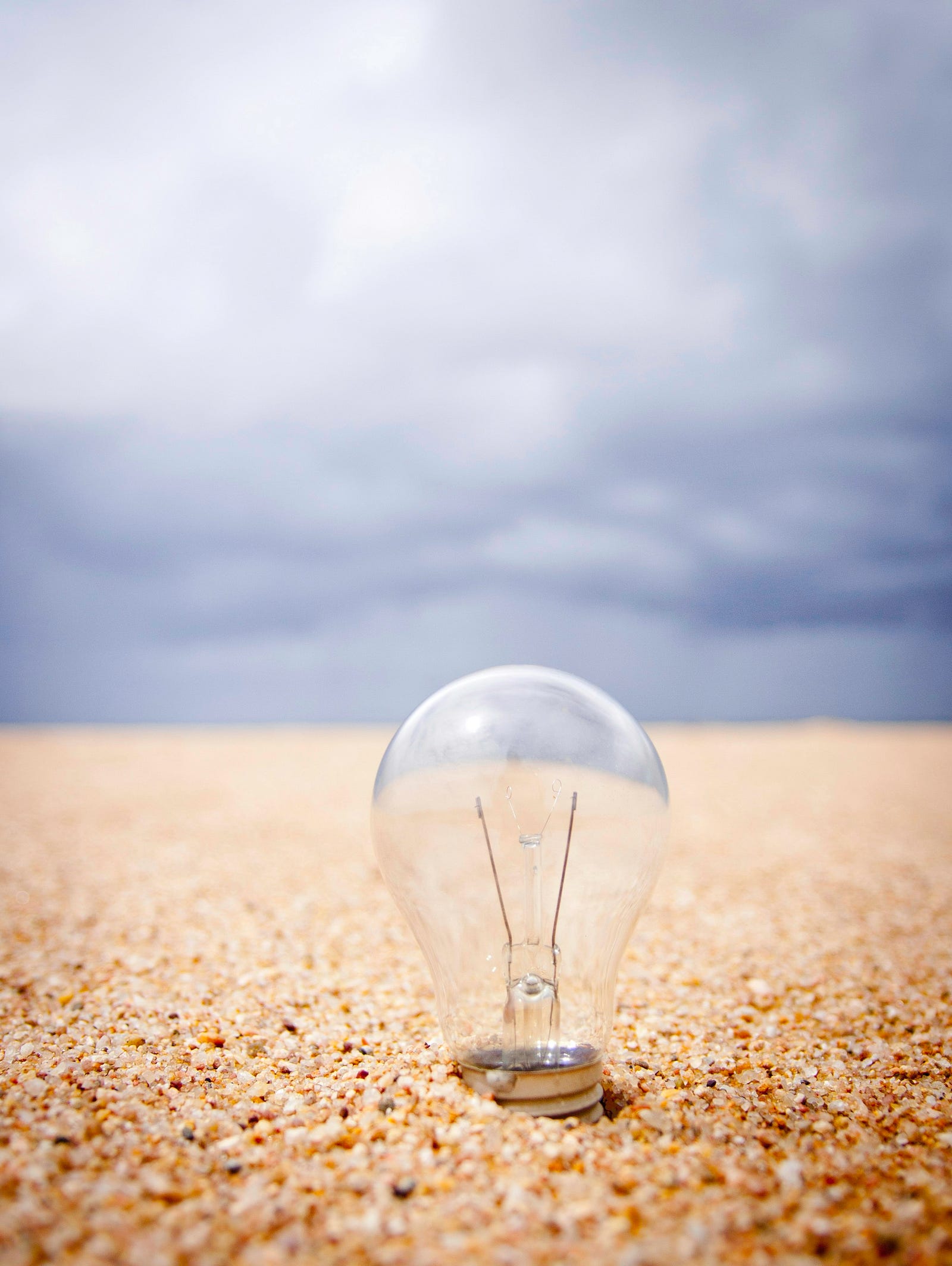 A lightbulb sticks up out of the sandy beach. A cloudy sky is in the background.