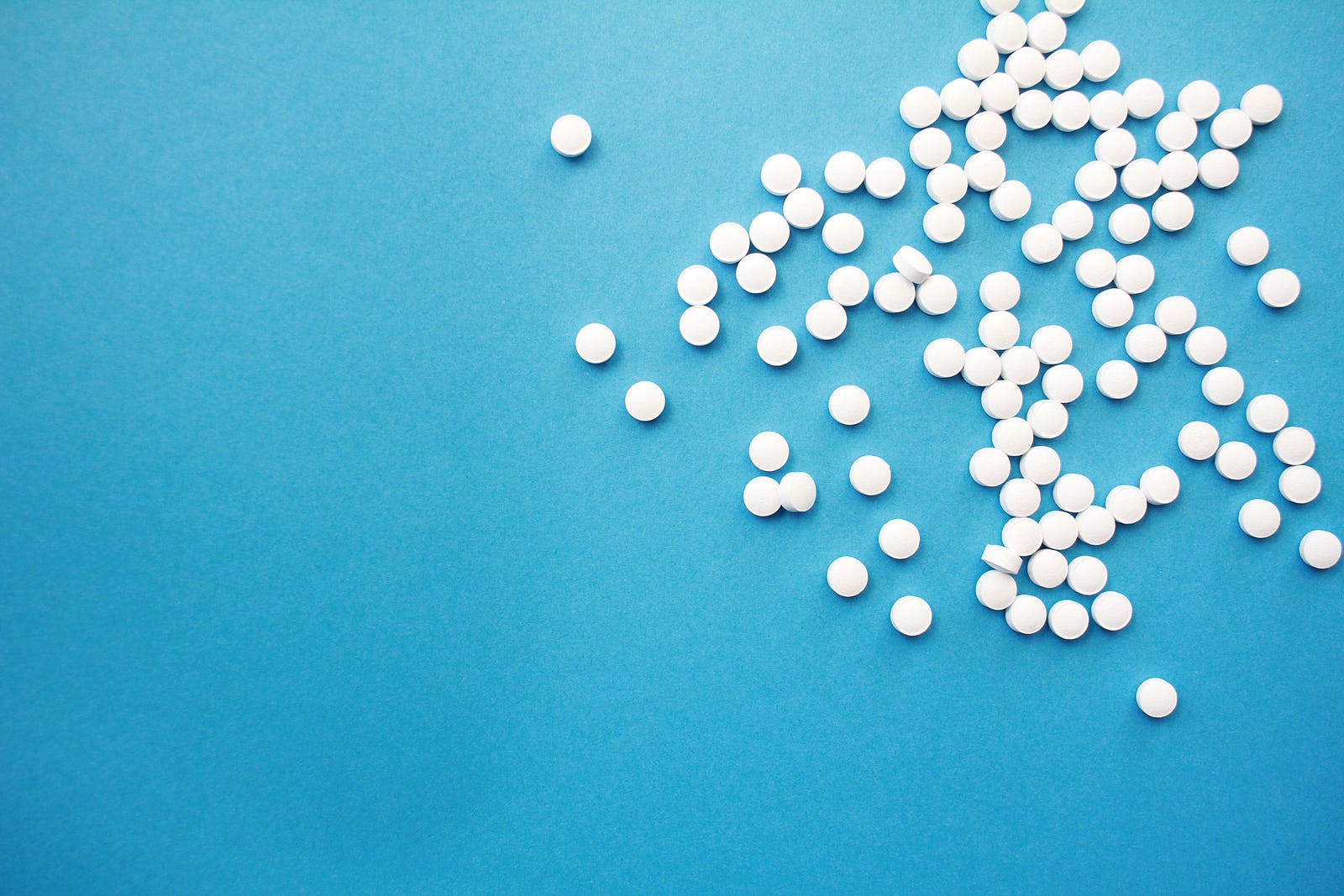Dozens of white tablets are strewn across a light blue background. Second, a meta-analysis published in The Lancet in 2010 found a one-quarter (24 percent) reduction in colorectal cancer incidence among individuals who took aspirin regularly.