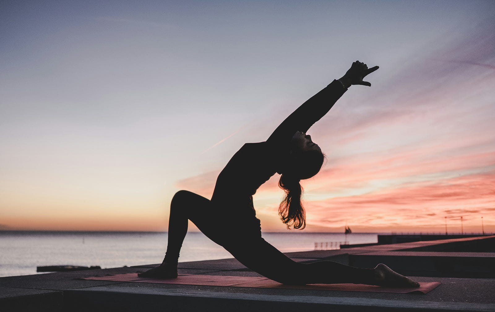 A woman does yoga on the beach at sunset.