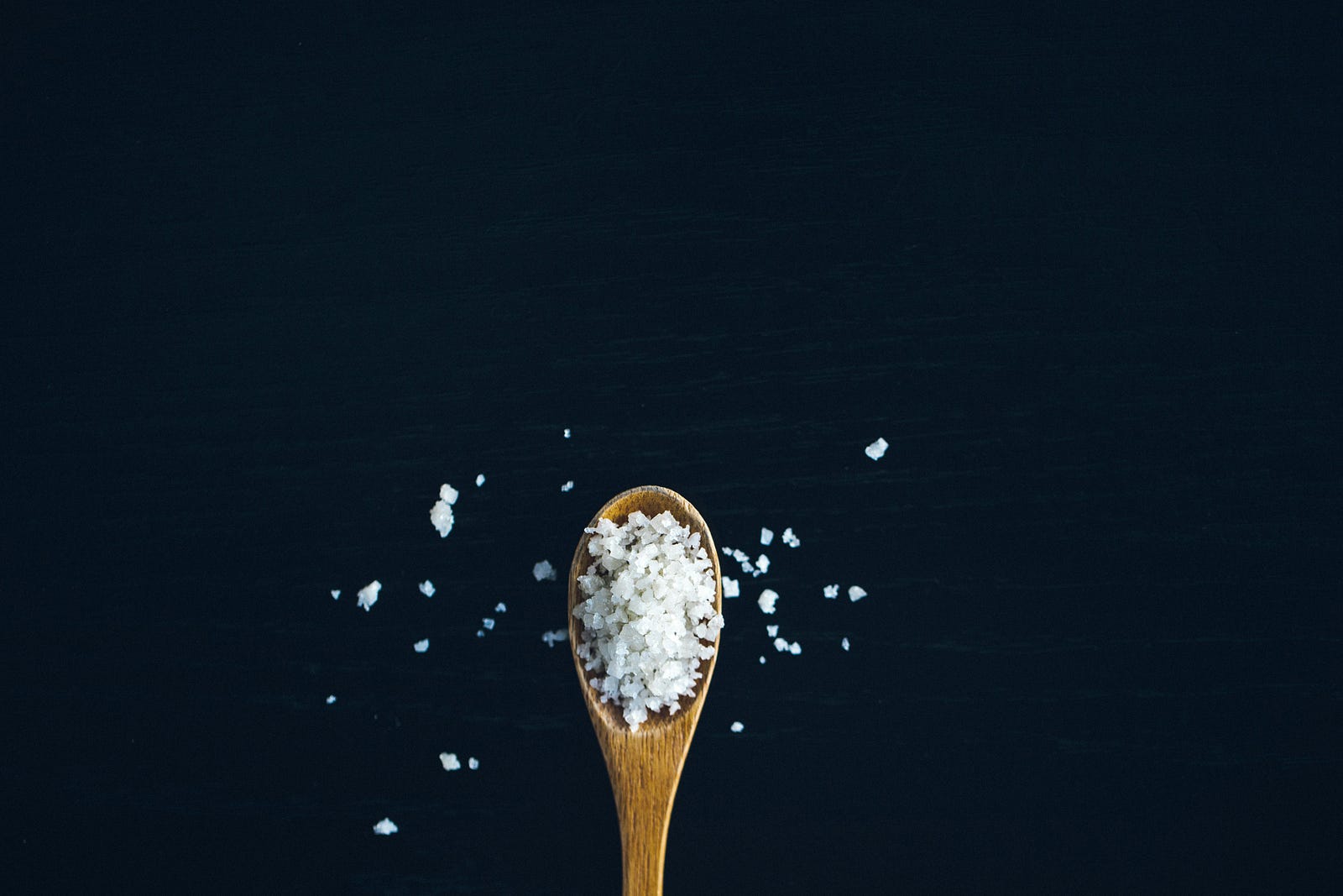 A small wooden spoon emerges from the bottom of the image, holding coarse salt.