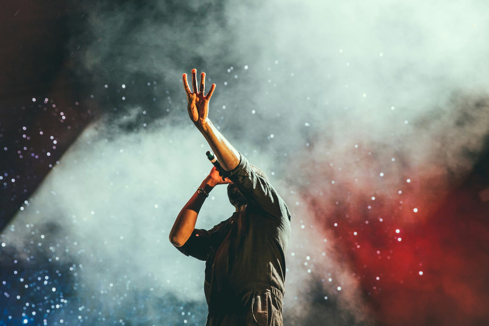 A concert singer brings a microphone to his mouth as he extends his left arm skyward.