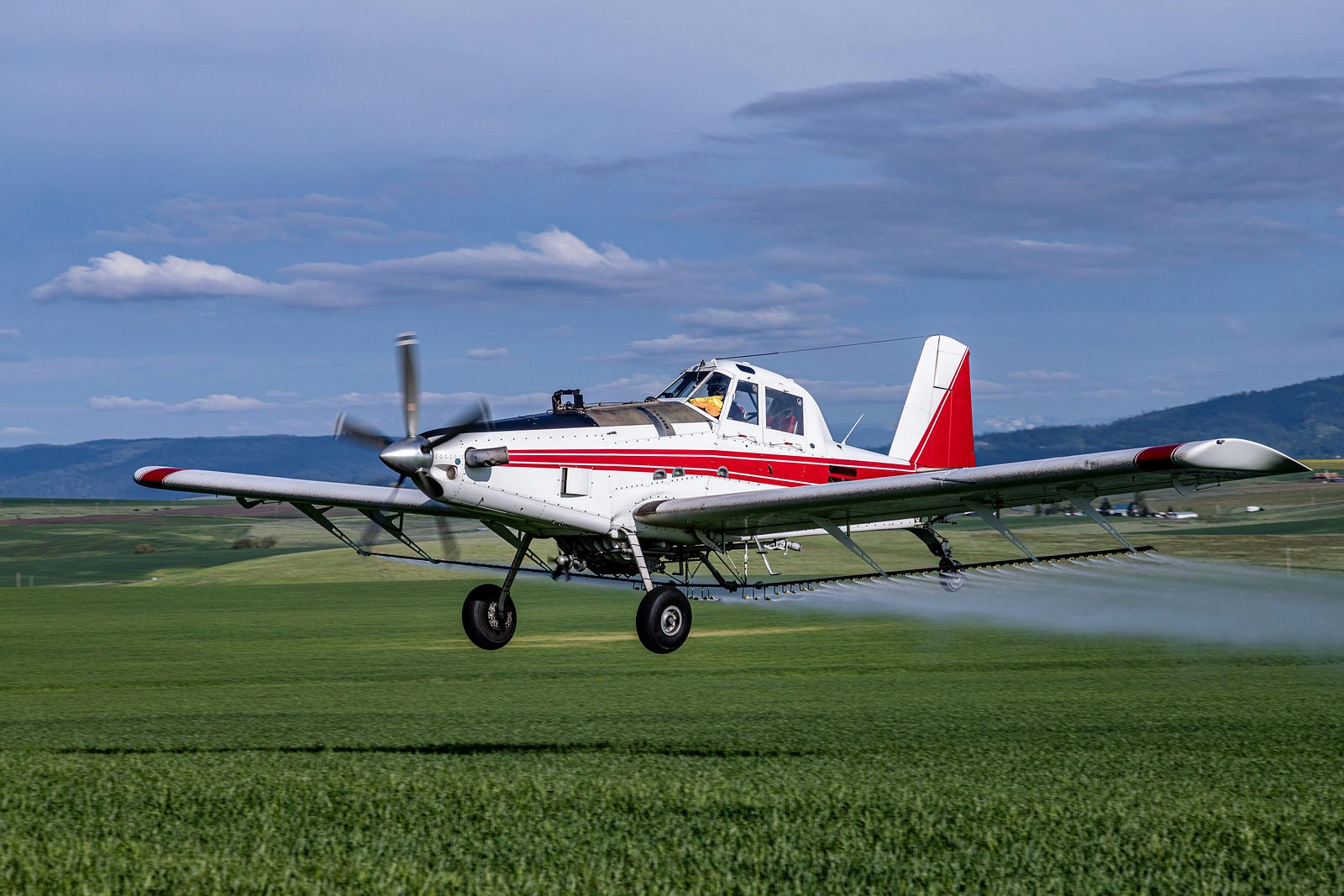 An airplane sprays pesticides on farm crops.