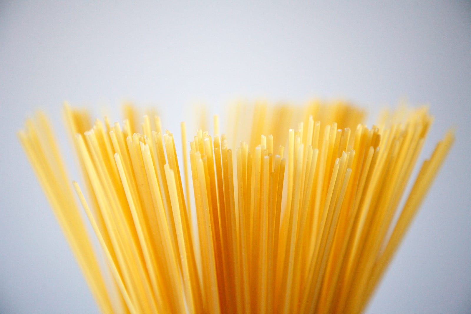 The ends of dry, uncooked spaghetti stick up into the image. Light gray background. Begin with one gram of carbs per pound of body weight to lose fat. Use two grams to gain.