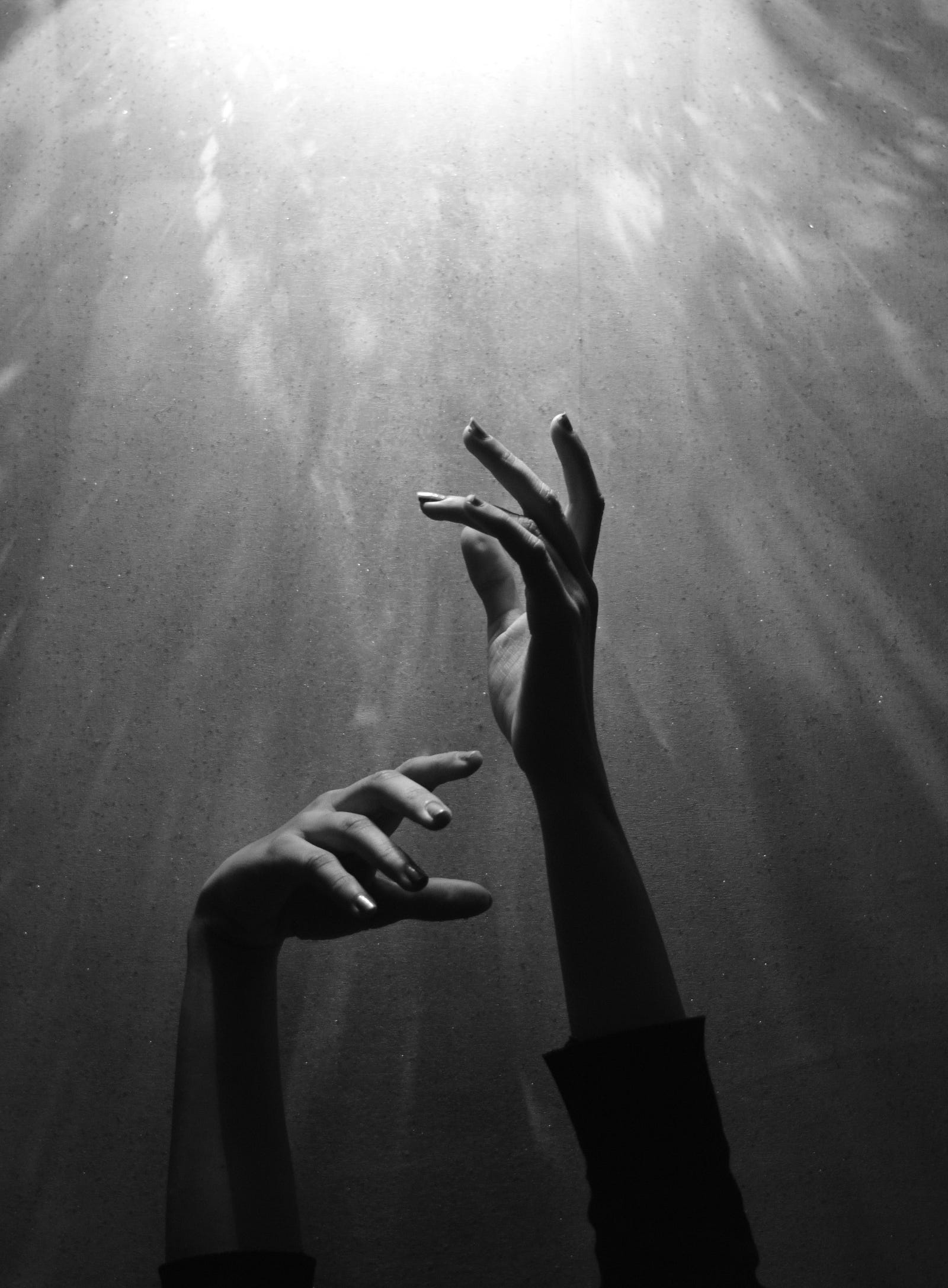 Two underwater arthritic hands reach upward. Black and white image.