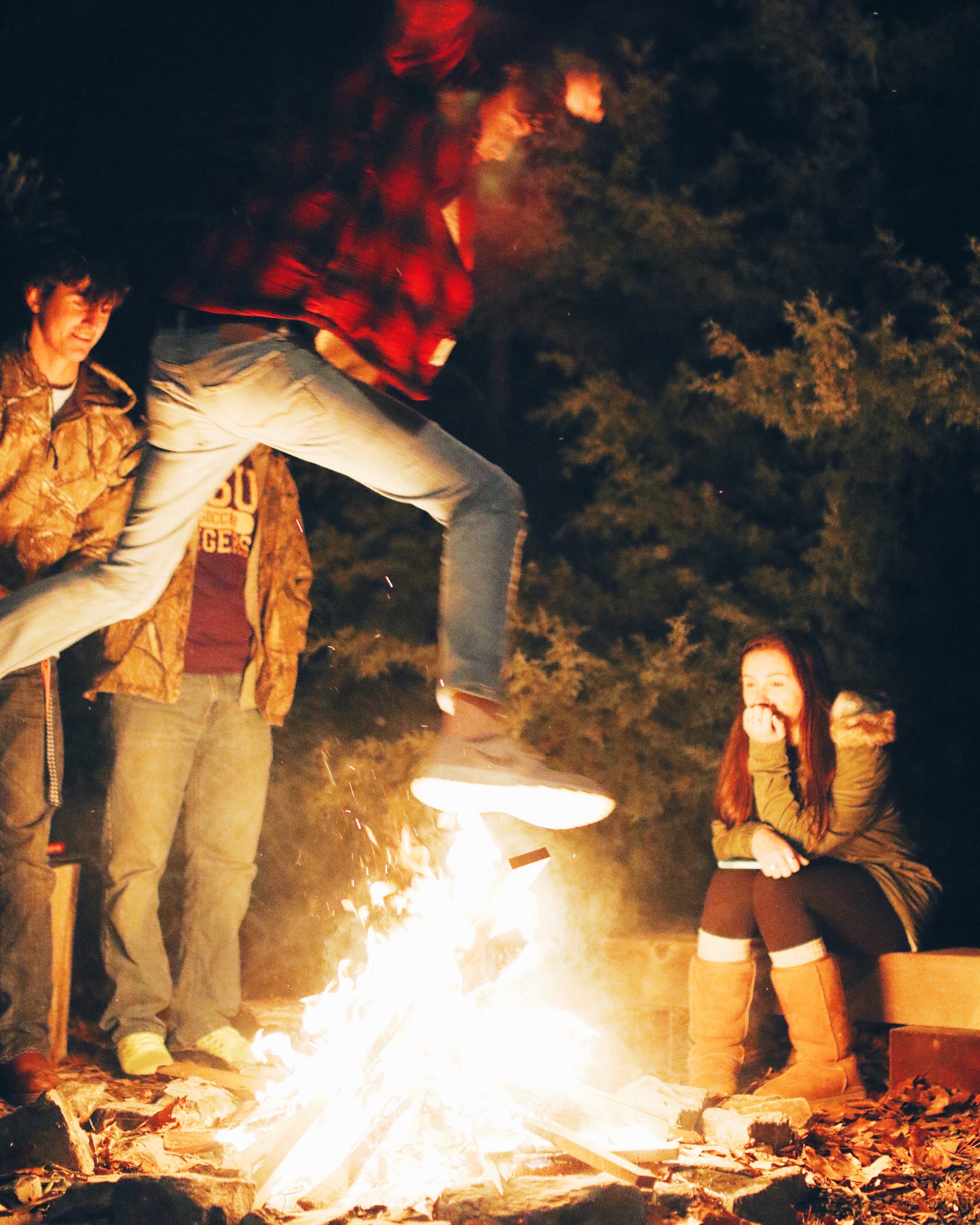 Guy jumping over a fire with people watching.