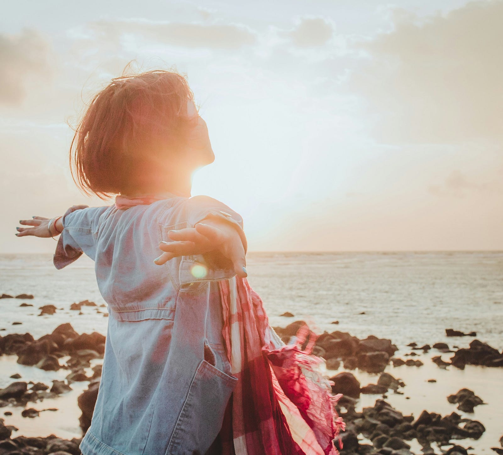 A woman opens her arms broadly as she stands in front o a rising sun.