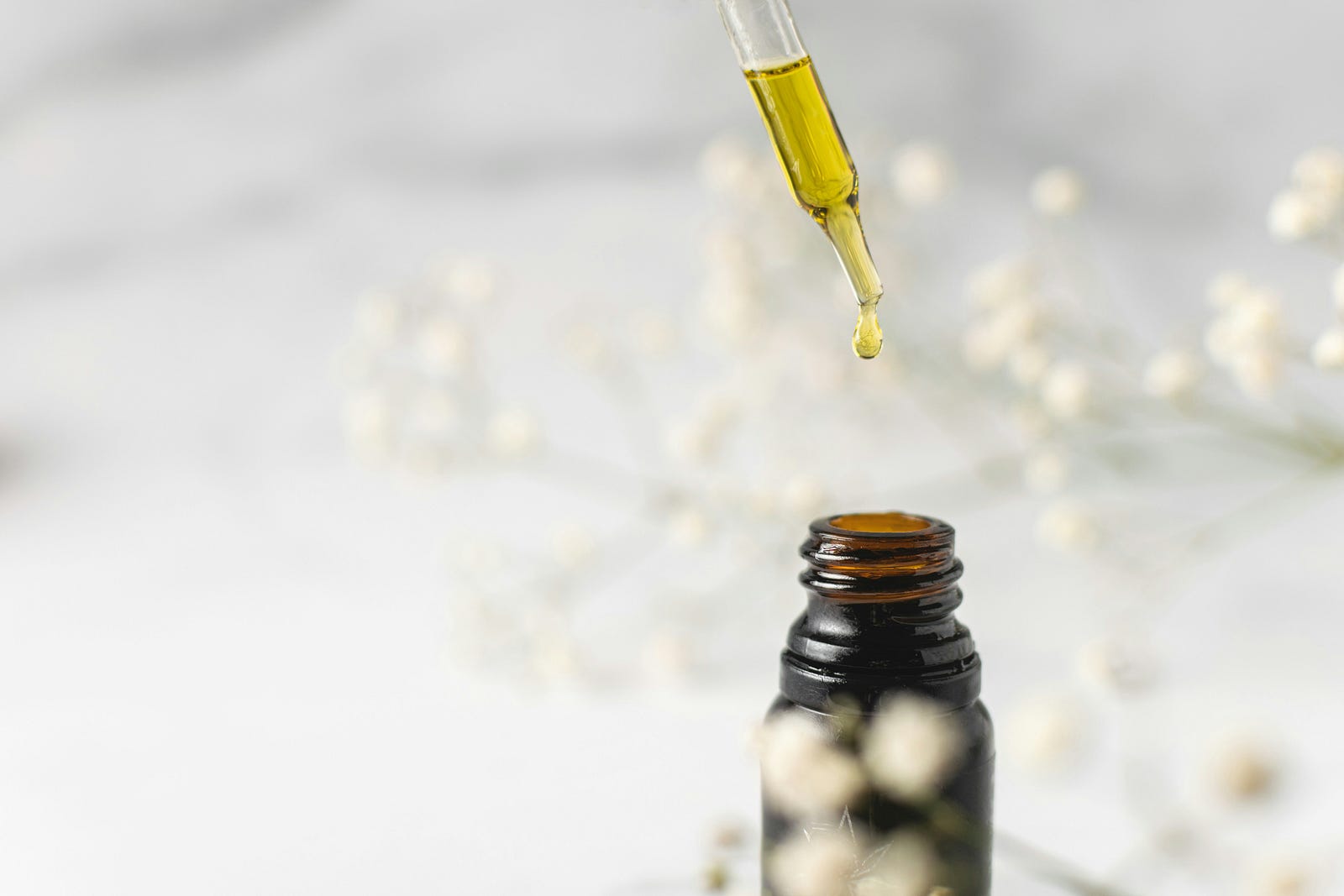 An eye dropper lifts drops of a yellow-colored essential oil from a small bottle.