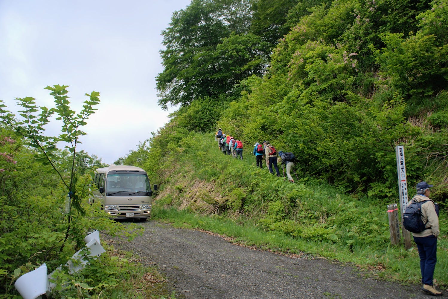 Hikers start walking along the hill at the Hanesawa Trailhead to Yozo-san as a bus waits nearby.