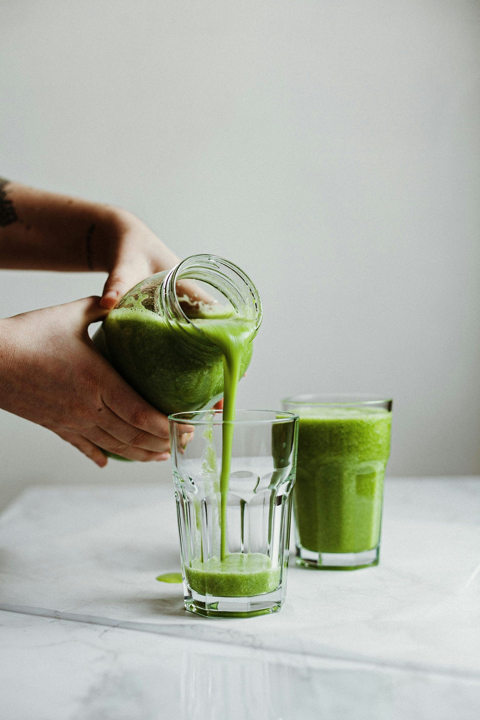 Someone pours green juice from a Mason jar into a glass.