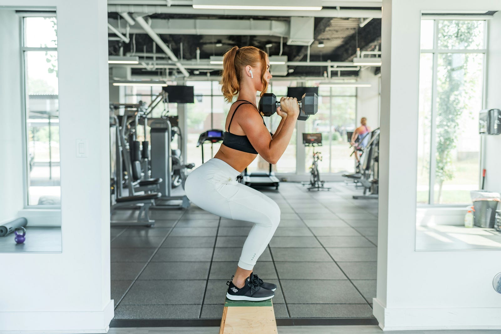 A woman performs a squat (with dumbbells) in a gym.