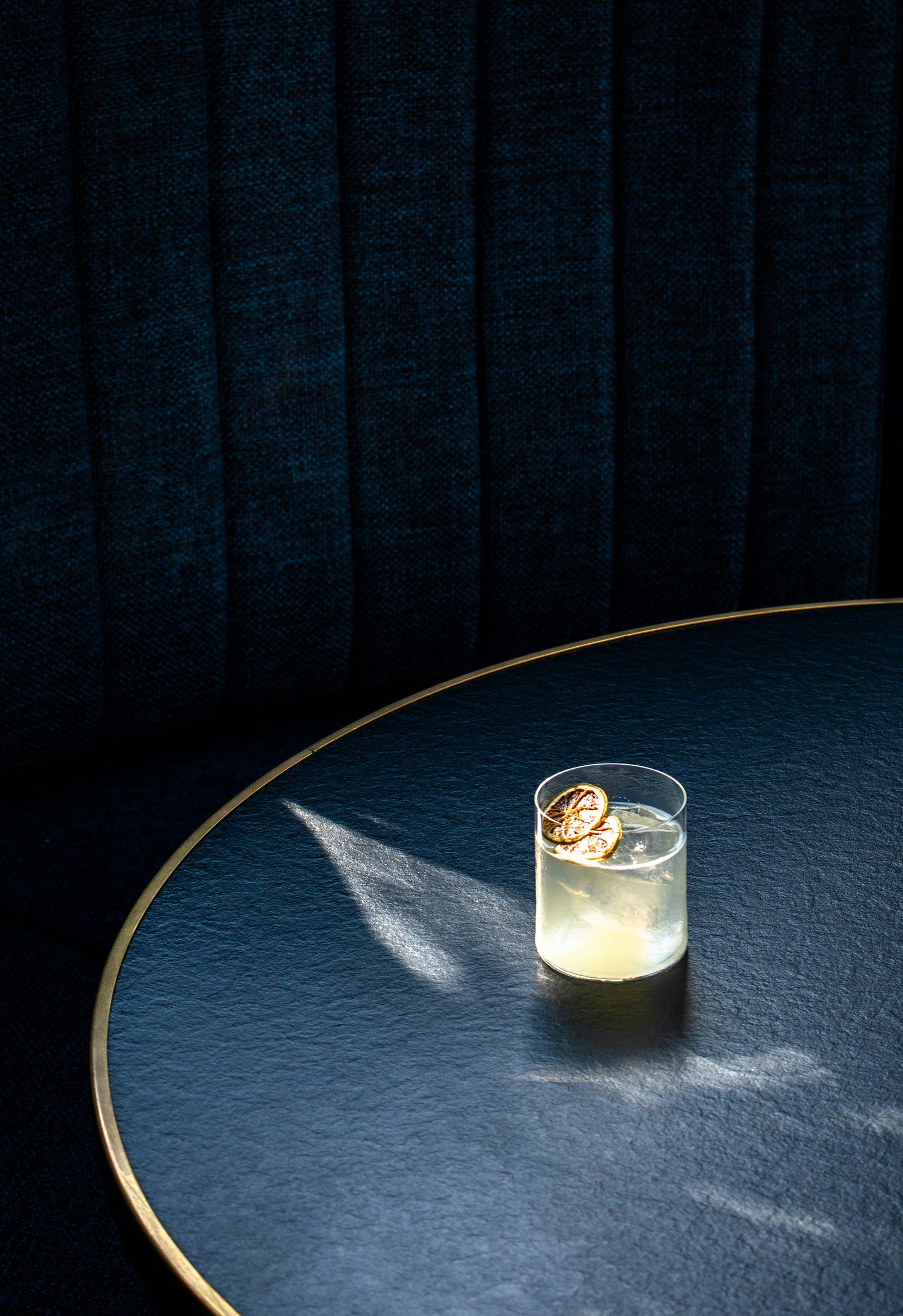 A glass of clear alcohol perches towards the left side of a round, blue table.