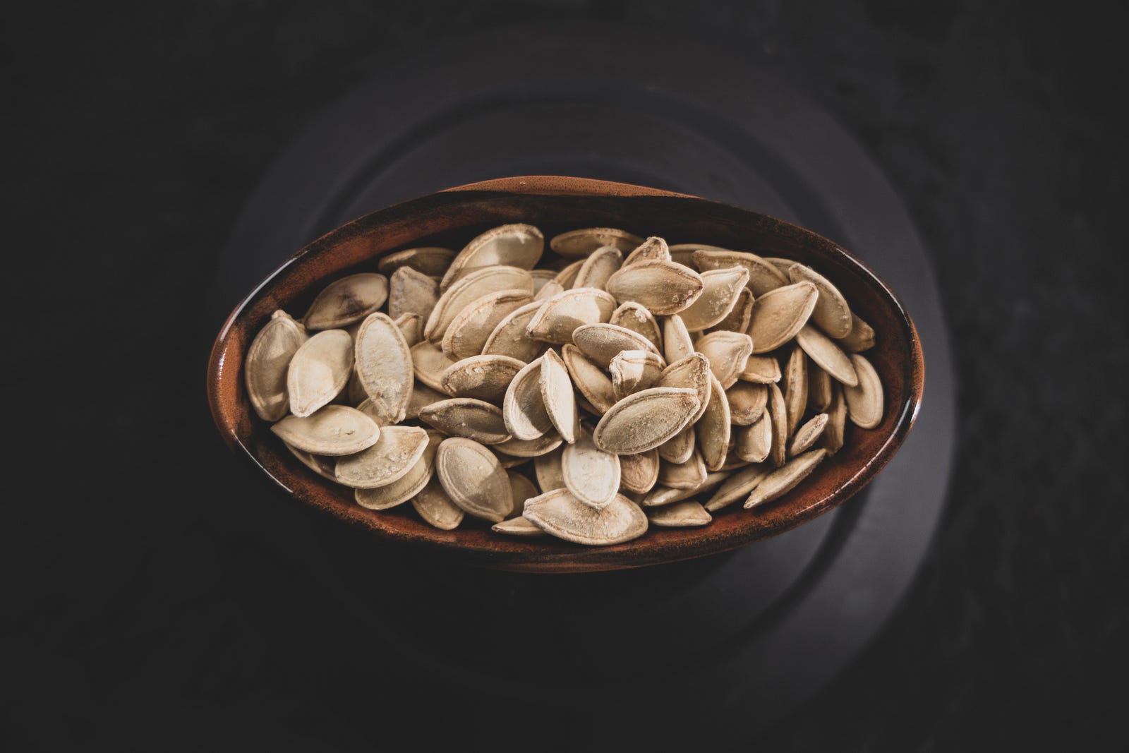 Pumpkin seeds fill a shallow wooden bowl (black background). Pumpkin seeds are rich in magnesium.