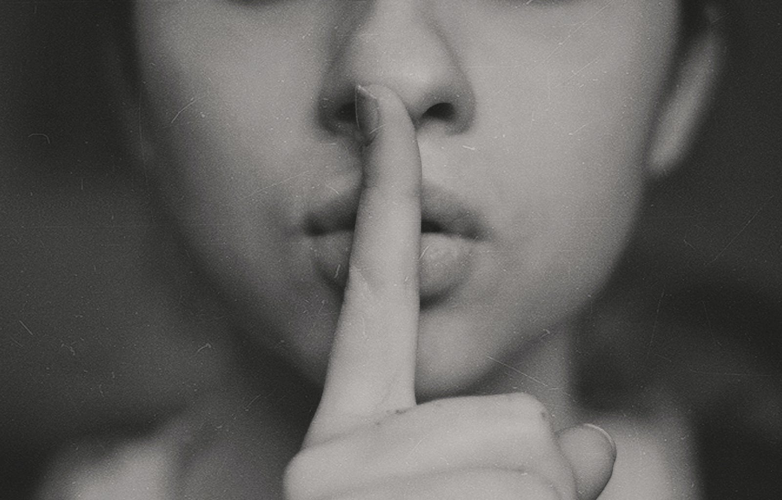 A black and white image of a person putting their second digit to their mouth, signaling “Shh.” Silent walking might be worth exploring if you find solace in quiet reflection, yearn for a respite from the daily cacophony, or seek a novel way to connect with others.