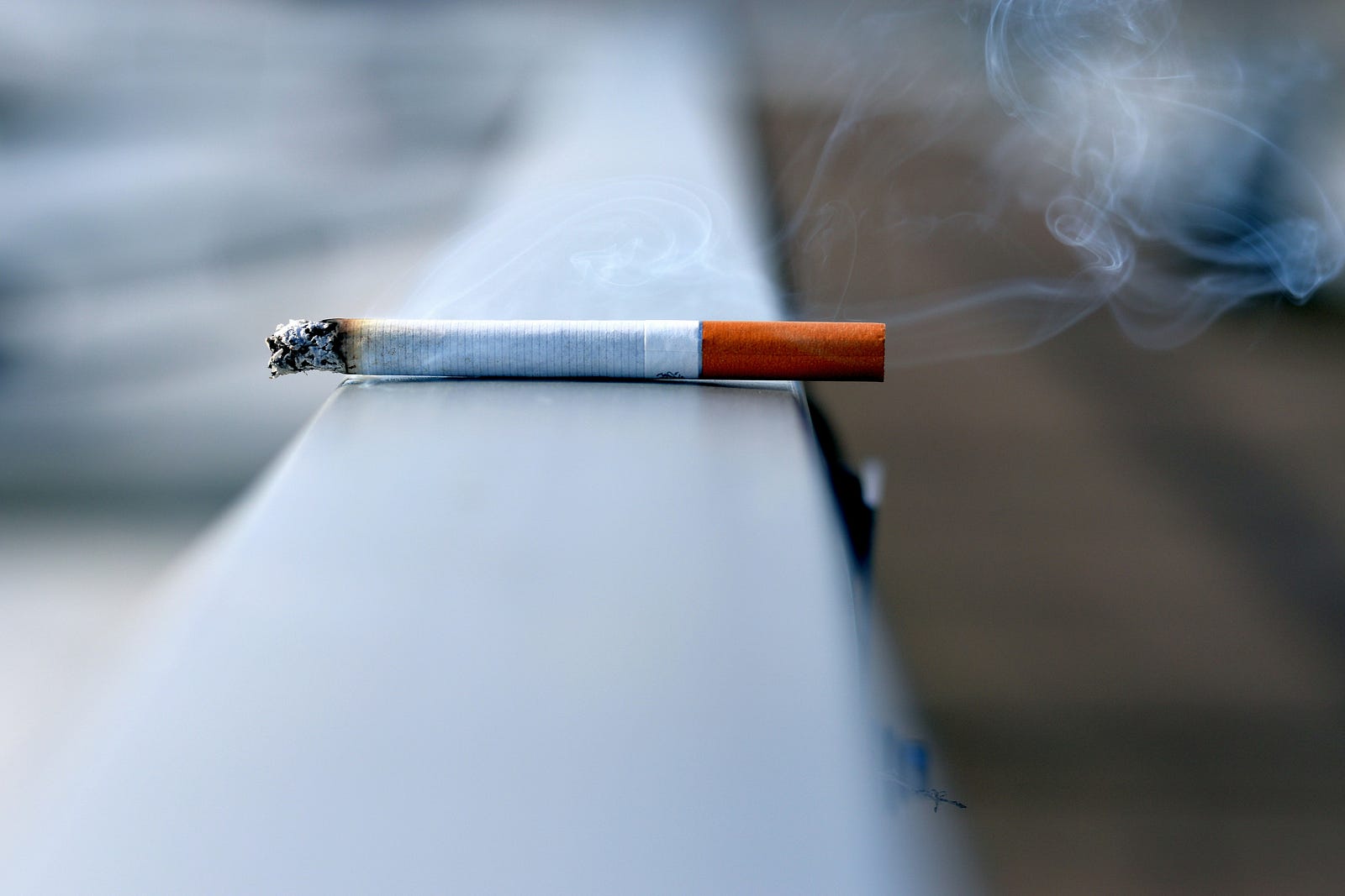 A single burning cigarette sits on a rail. Tobacco increases dementia risk.