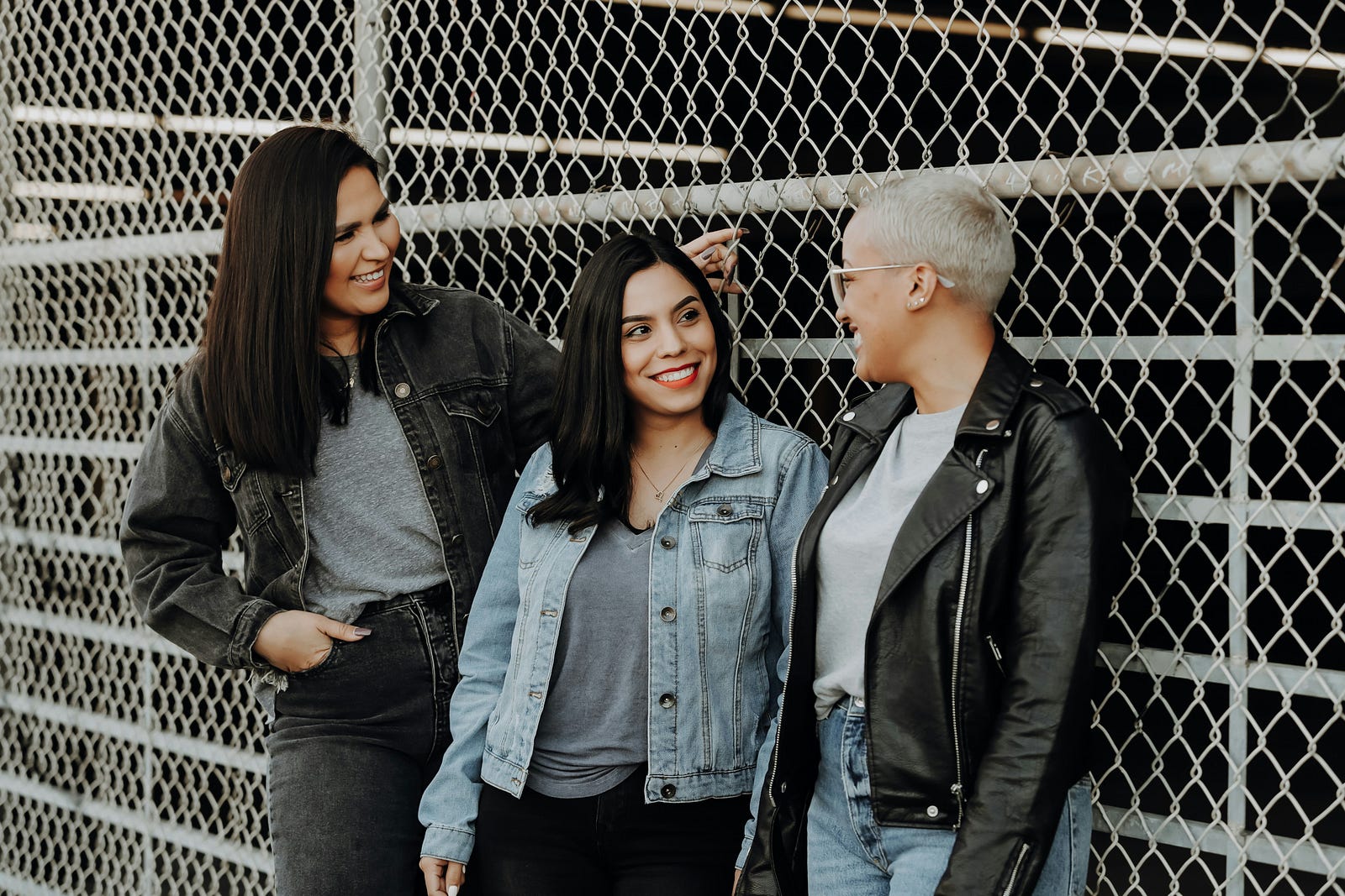 Three middle-aged women stand in front of a fence.