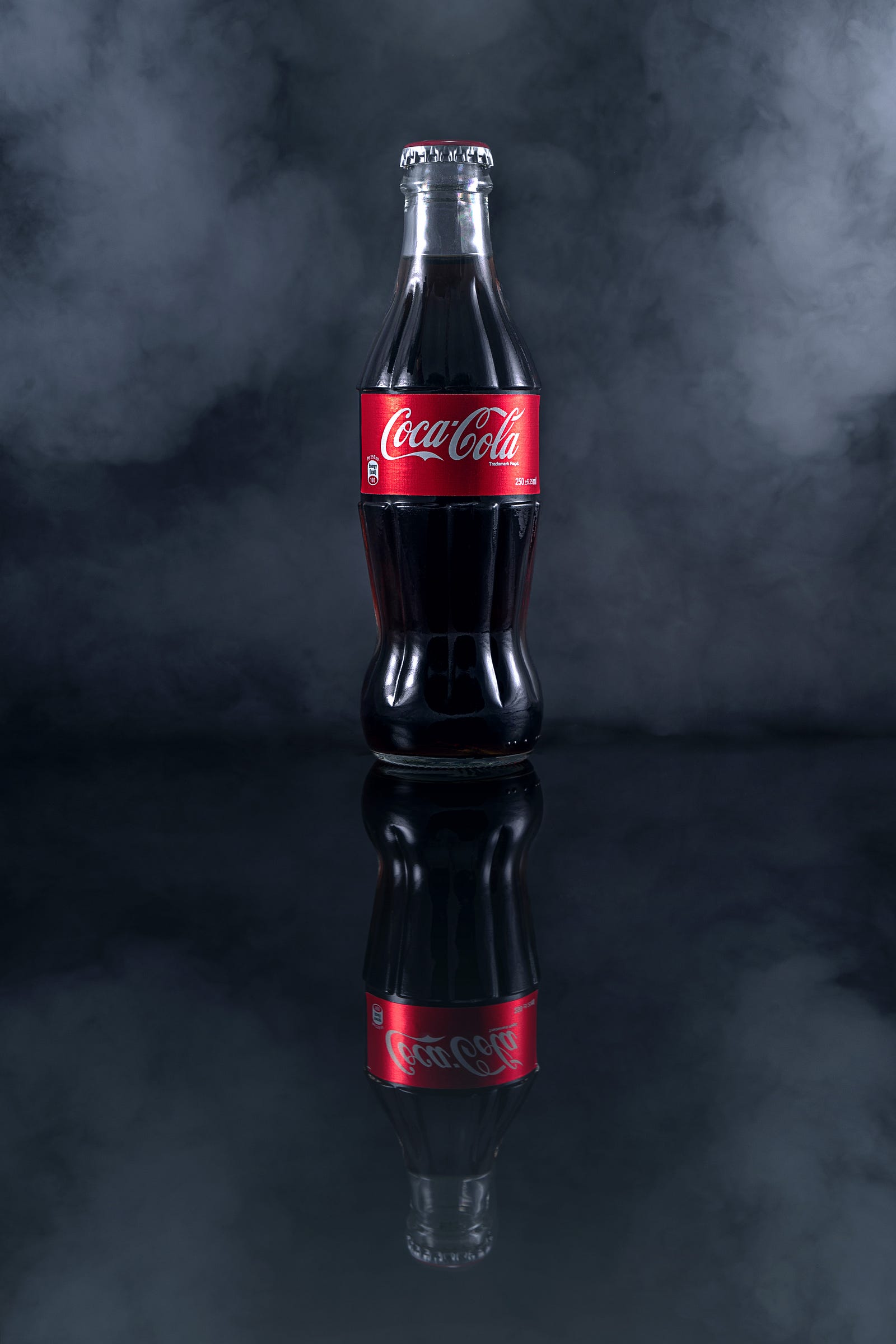 A lone bottle of Coca-Cola sits on a dark blu surface (wth w bluish-white wall behind). When it occurs, coffee withdrawal typically begins 12 to 24 hours after caffeine cessation.