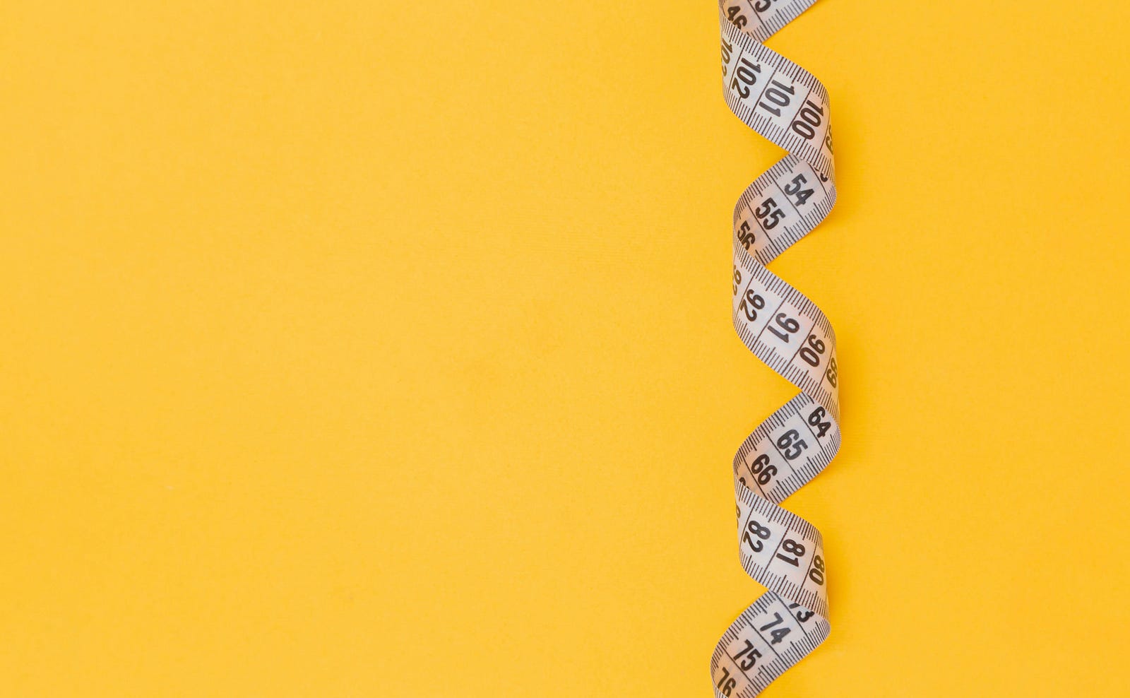 A twisted flexible tape measure against a mustard-colored background.