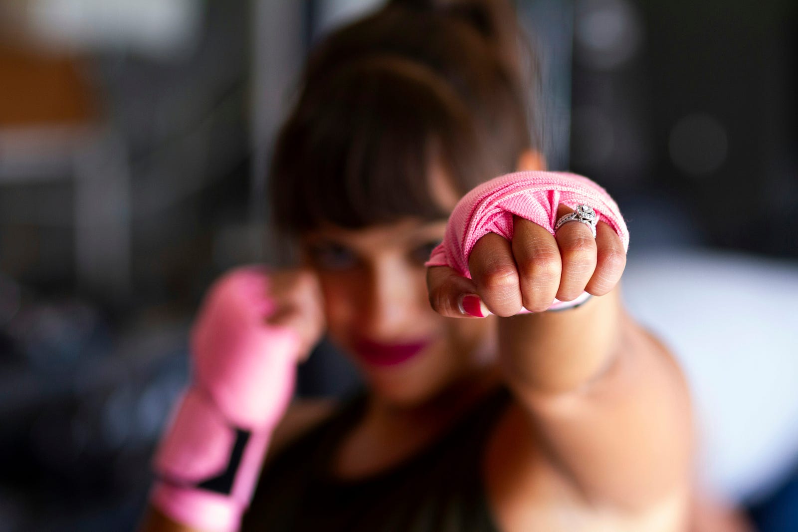 A young woman in pink fighting gloves punches her left arm forward.