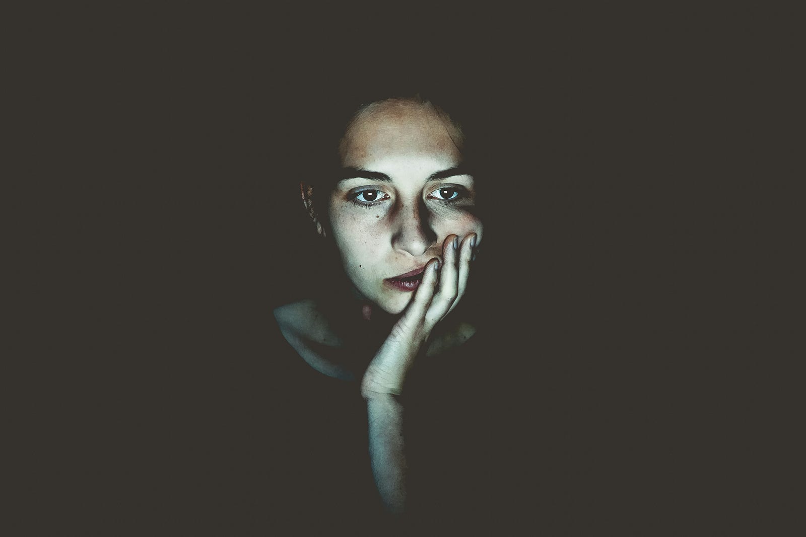 A woman appears tired as she faces us, her left hand holding her face.