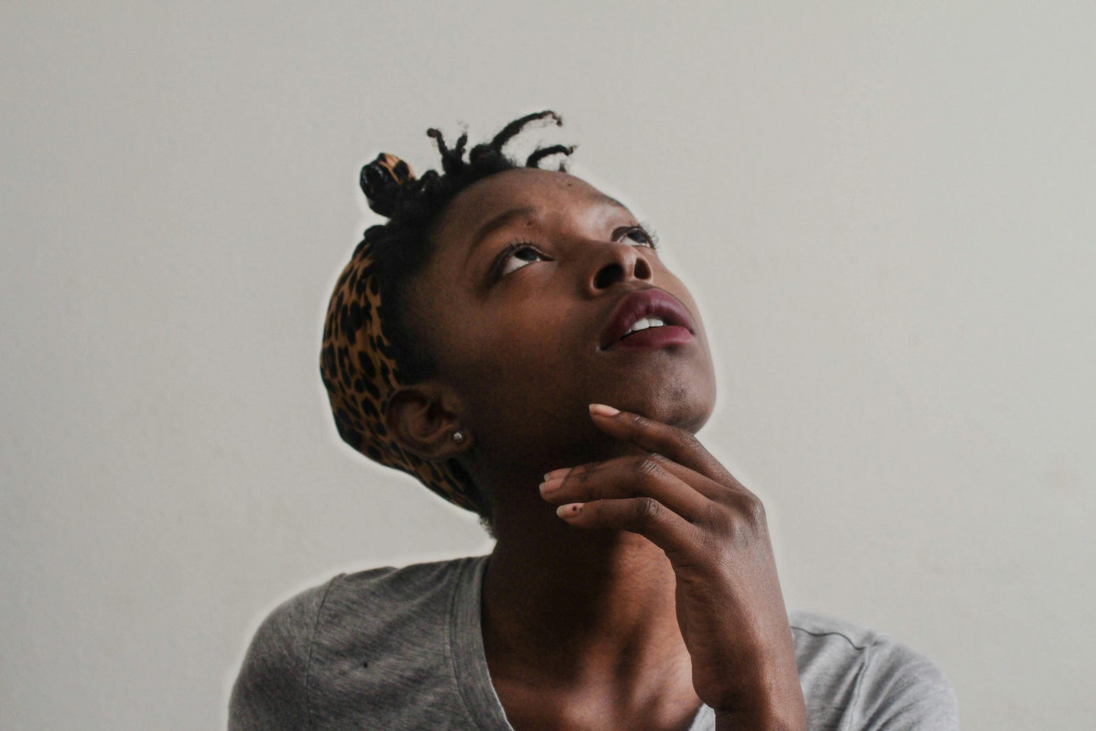 A young black woman looks upward, her right hand rising up to her chin.