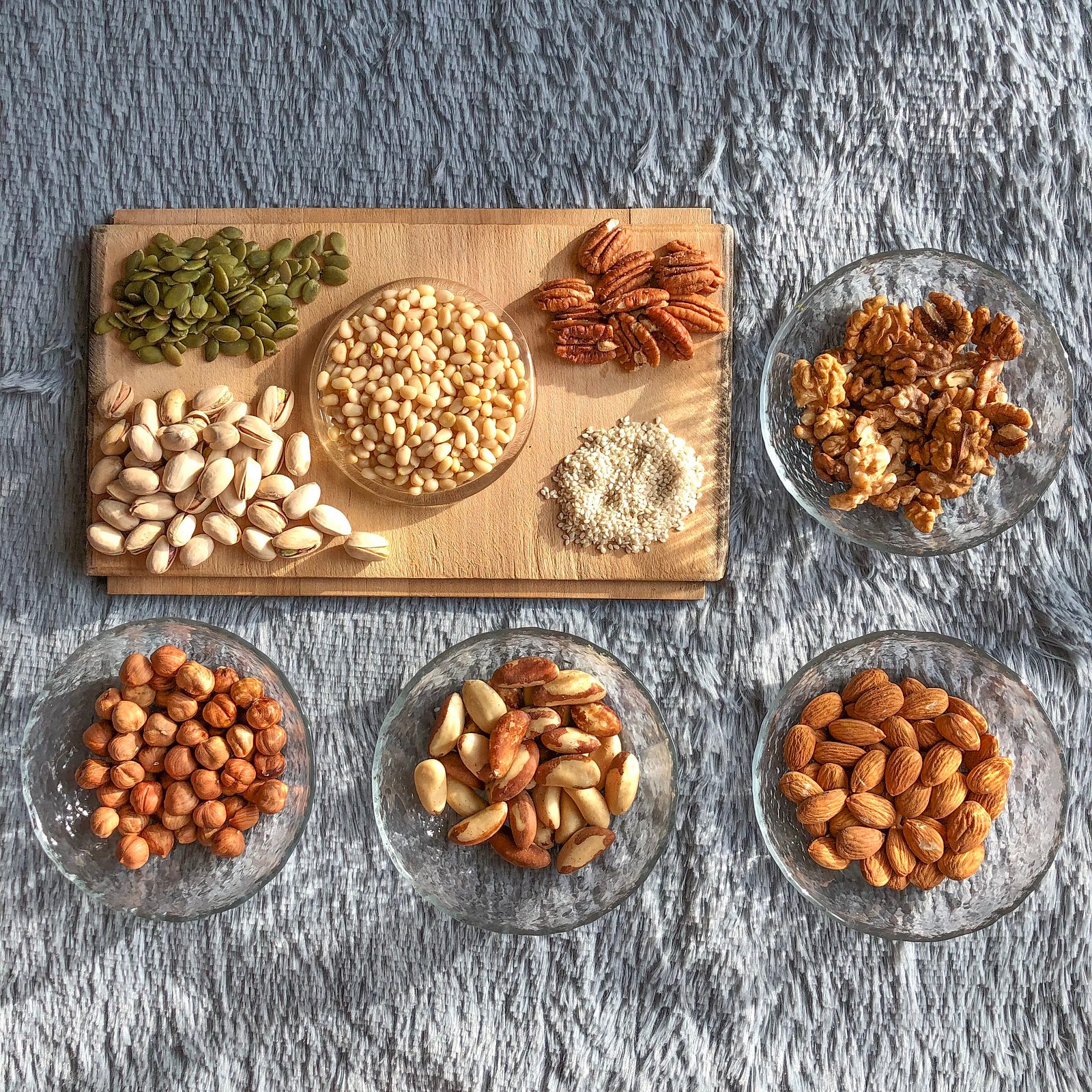 Various nuts sit in four small glass bowls. Theer is also a wood platter, in the upper left region, with more nuts. Addressing social and environmental factors is crucial in the fight against obesity.