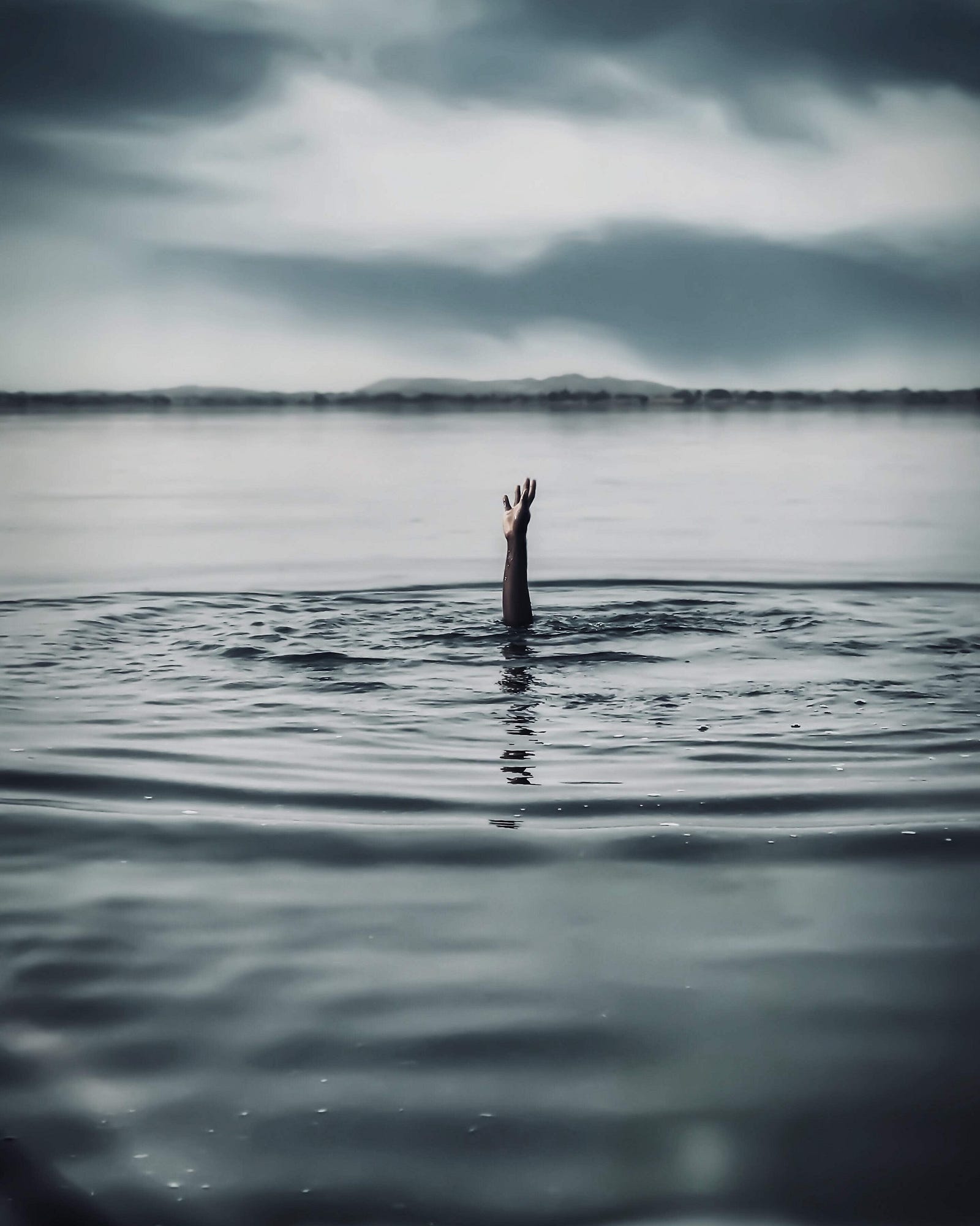 a hand reaches out of a large body of water — probably they are drwoning
