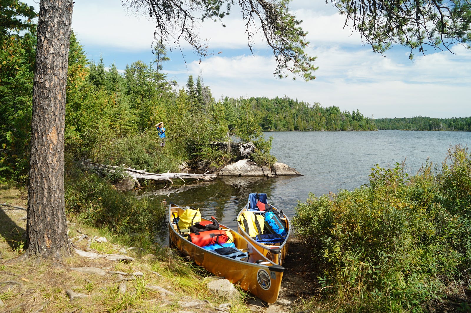 Two canoes with gear inside, on the edge of a waterway.