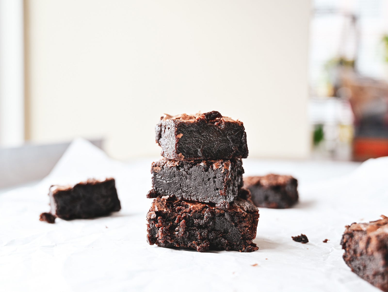 Three moist chocolate brownies stacked on top of each other on white parchment paper.