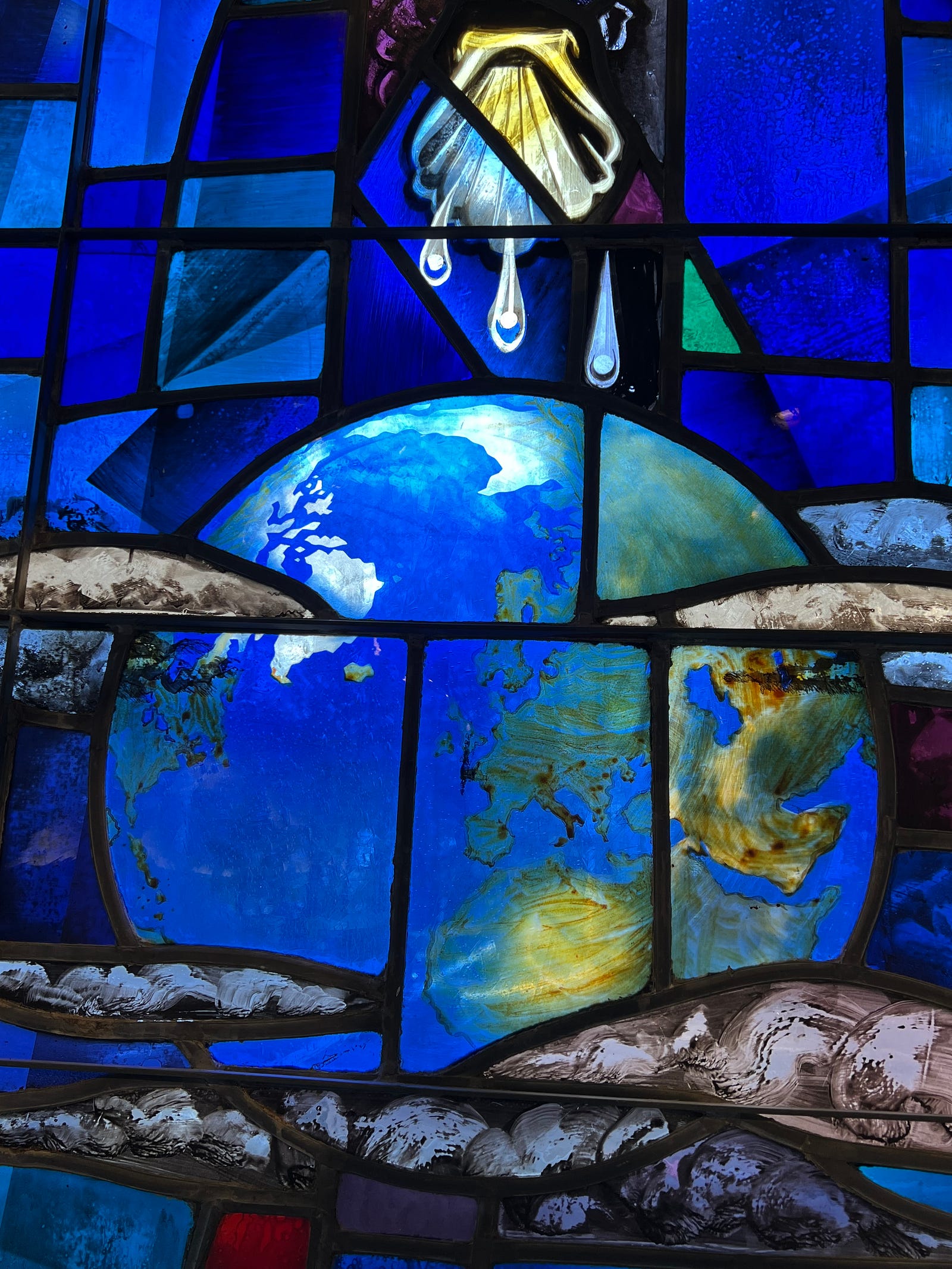 Photo of a piece of stained glass at St Andrew’s Madison, showing the Earth with the waters of Baptism dripping from a scallop shell above.